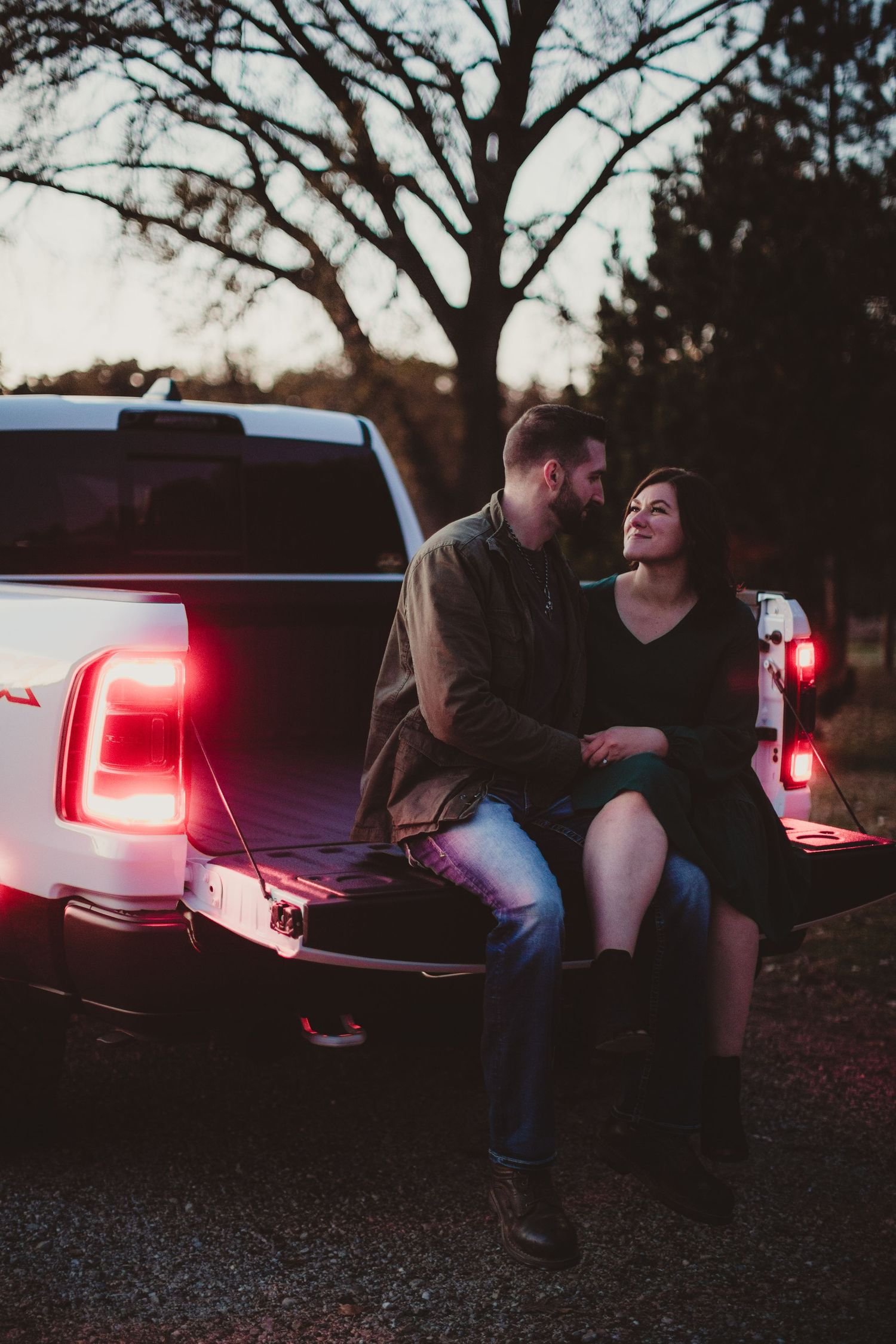 Couple sharing intimate moment on truck bed with tree silhouette in background.