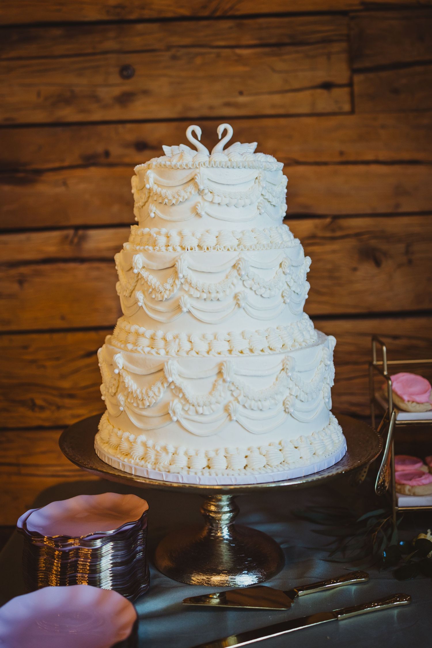 Classic four-tier white wedding cake with intricate piped lace details and swan topper on a silver cake stand.