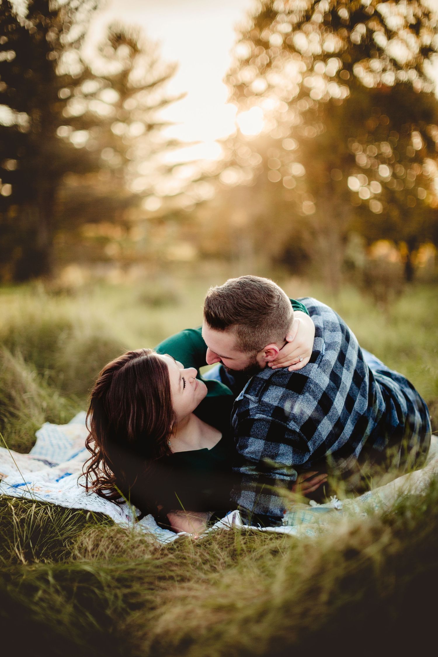 Couple sharing intimate moment on blanket in sunlit meadow.