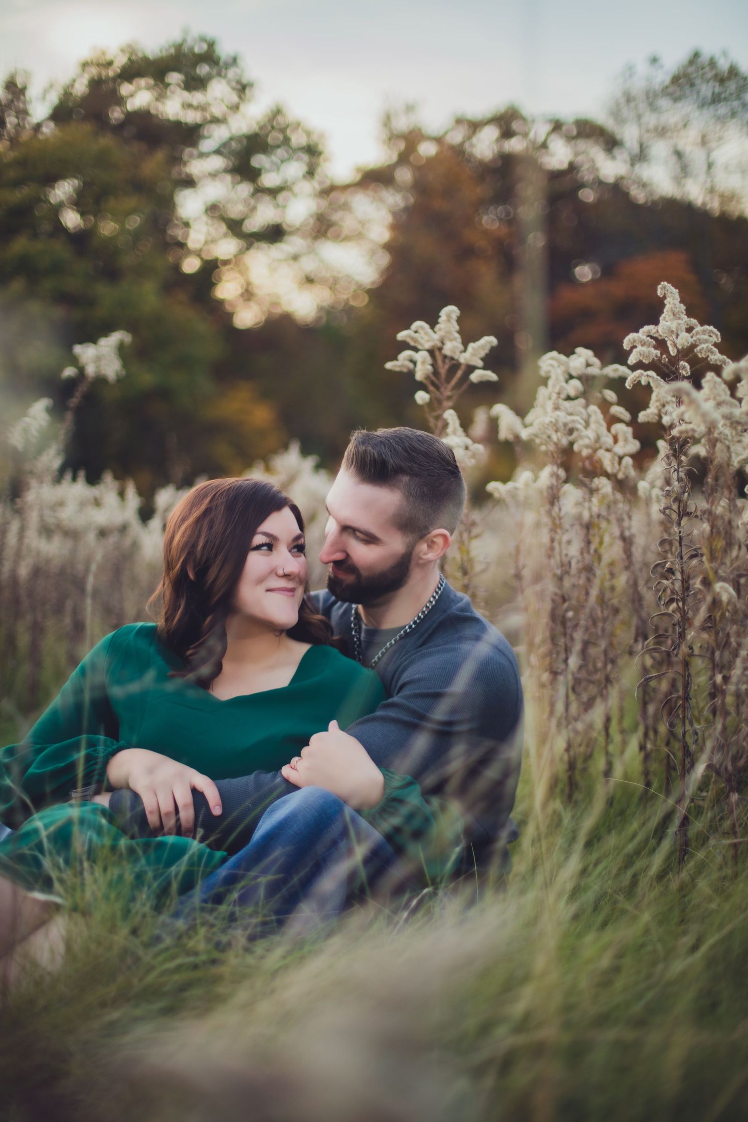 Couple in green and grey enjoying romantic moment in tall autumn grass.