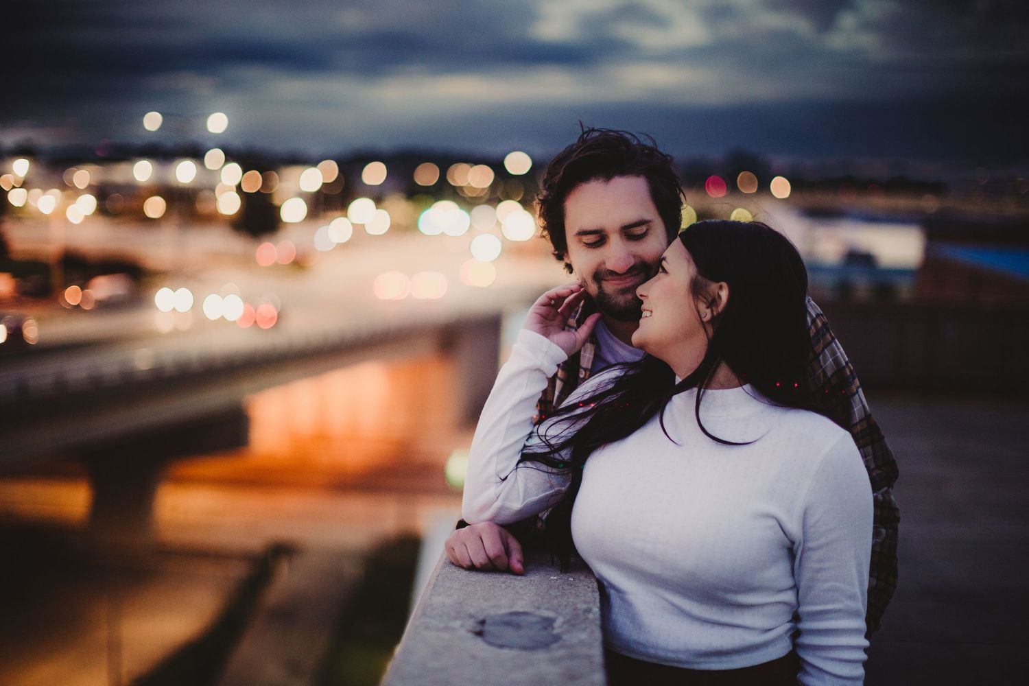 A romantic nighttime photo session with city lights creating a dreamy bokeh background.