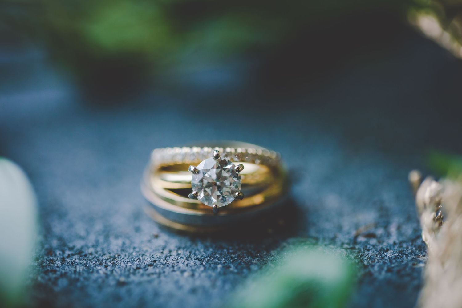 Close-up of sparkling diamond ring displayed with delicate greenery on blue surface.
