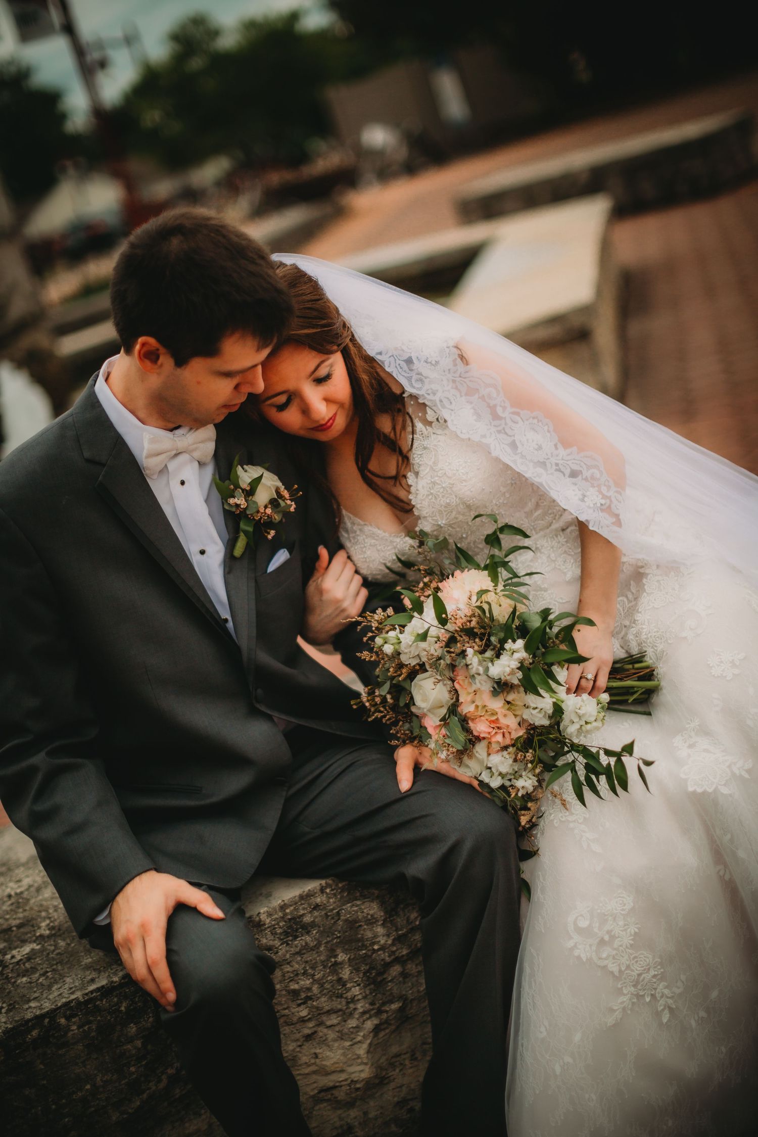 Intimate wedding photo captures couple sharing quiet moment outdoors with peach bouquet.