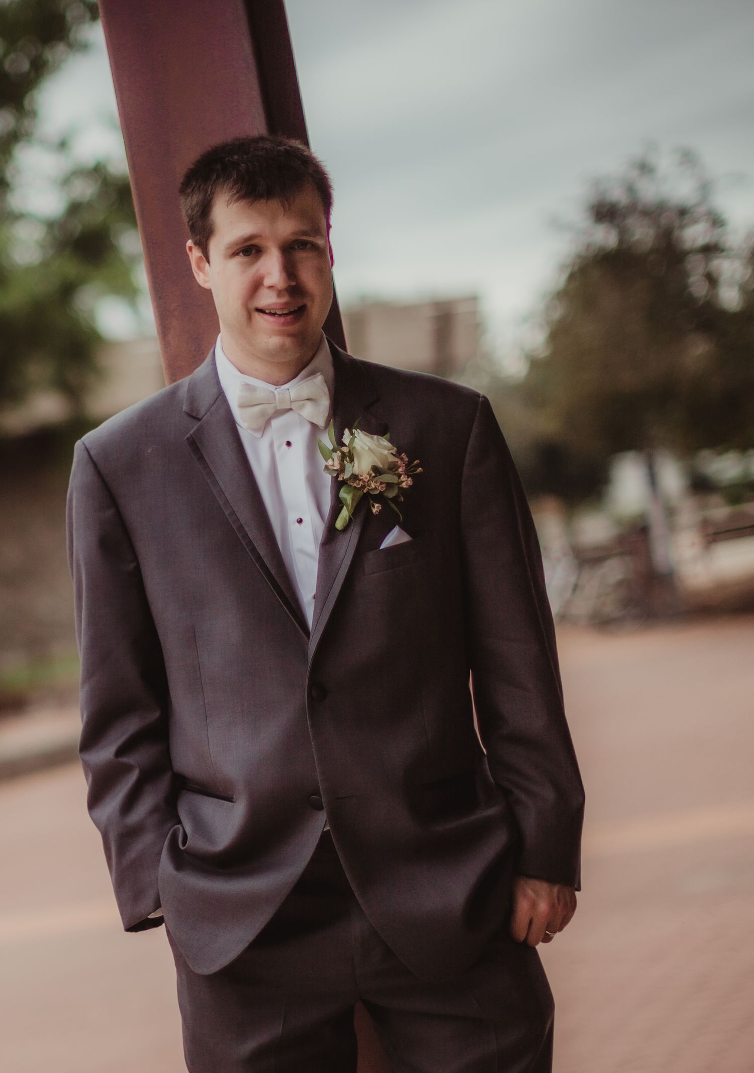 A groom in charcoal grey suit and bow tie poses for a formal wedding portrait.