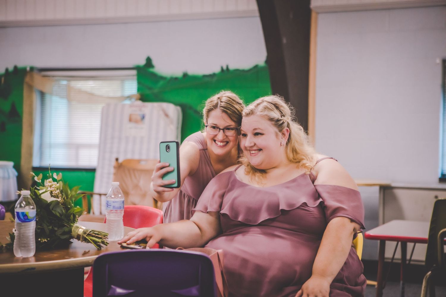 Two guests share a joyful moment while looking at phone during wedding celebration.