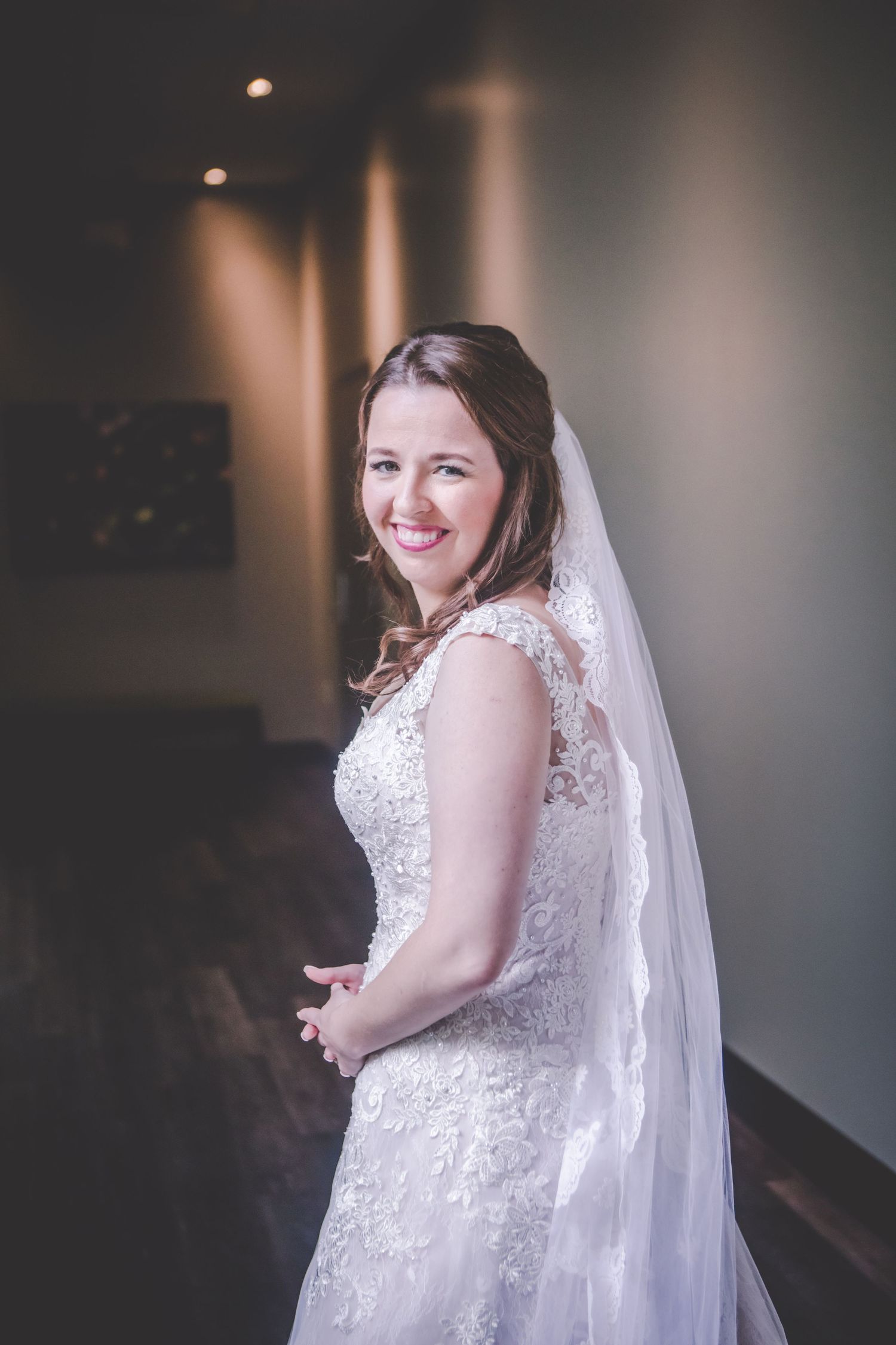 An elegant bridal portrait showcasing a detailed lace wedding dress and flowing veil in a modern setting.