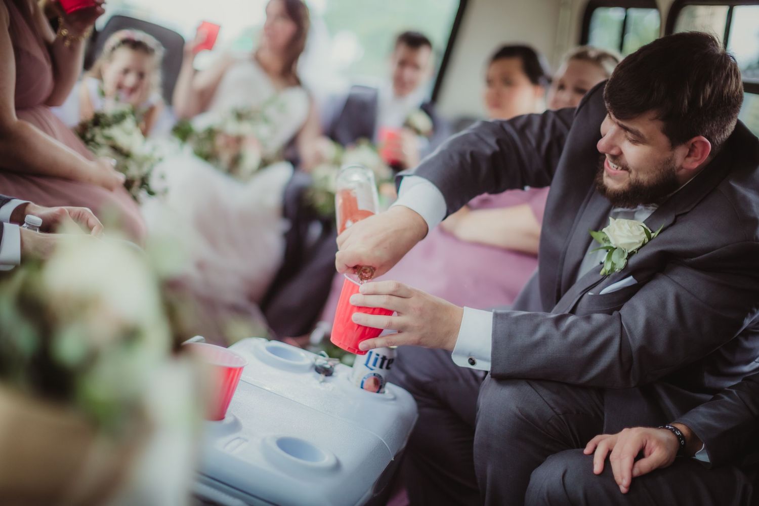 Wedding party member pours pink drinks into red cups on party bus.