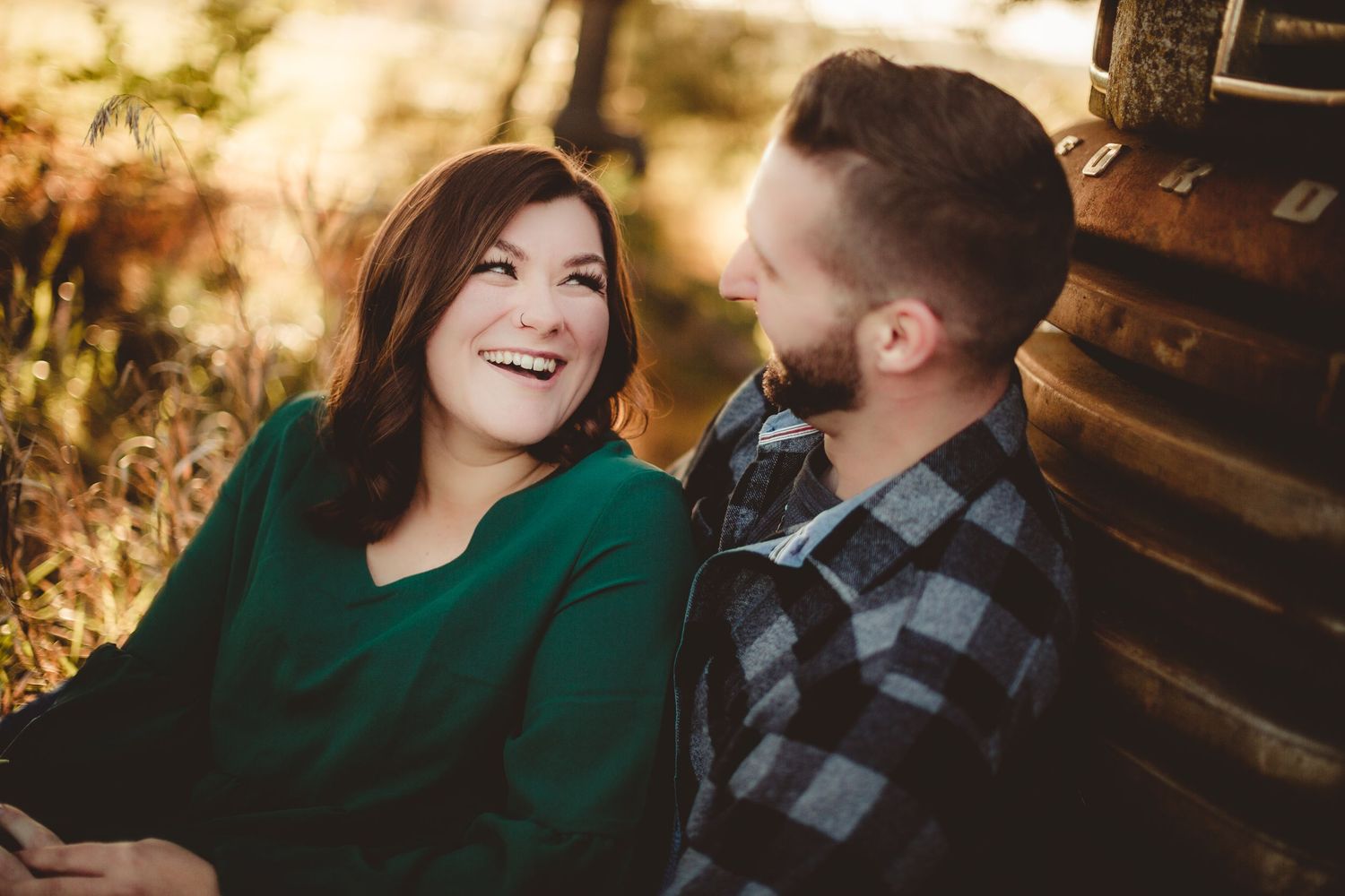 Candid moment of laughter between couple sitting by old truck during sunset.
