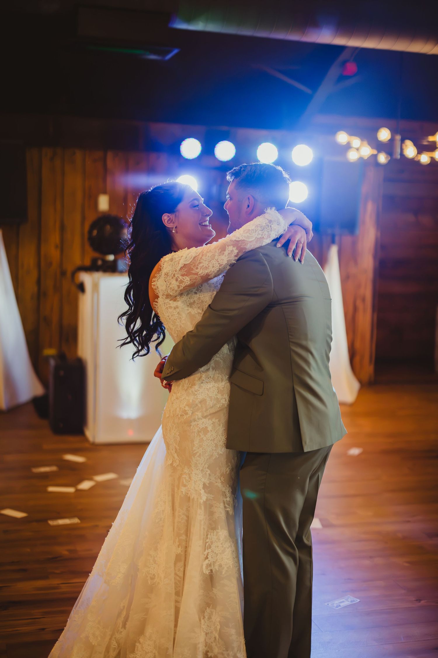 Bride and groom share their first dance in a rustic barn venue with warm stage lighting and string lights.