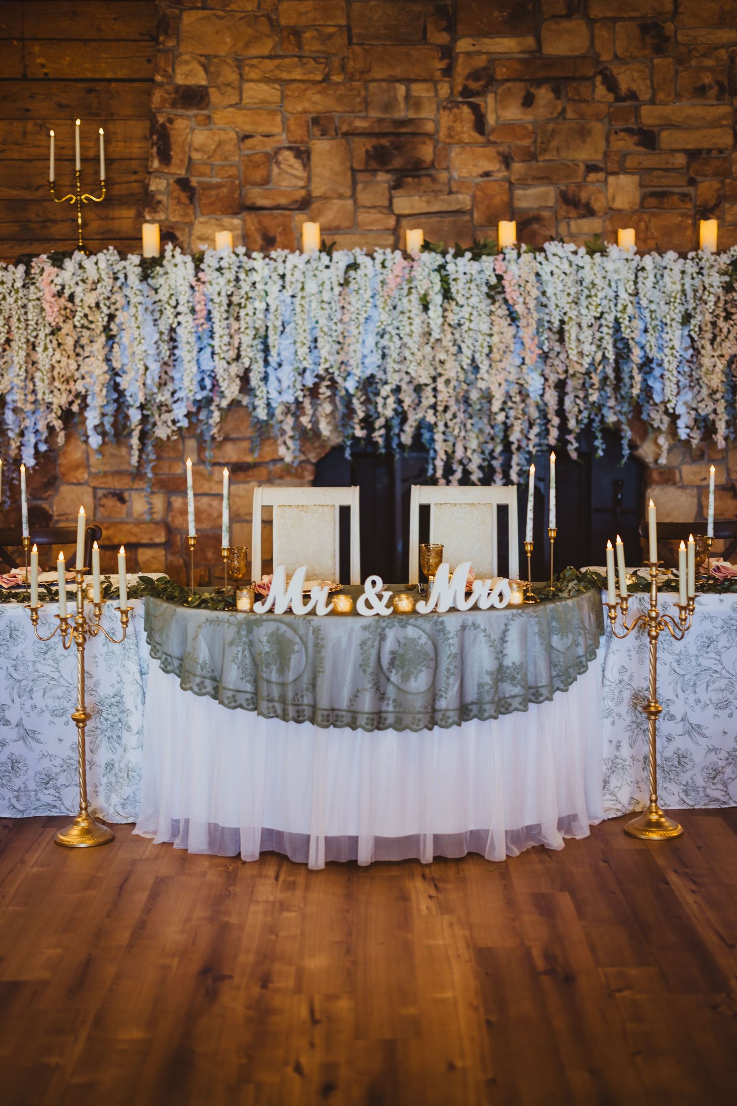 Elegant wedding sweetheart table with Mr. & Mrs. sign, gold candelabras, and cascading white floral backdrop.