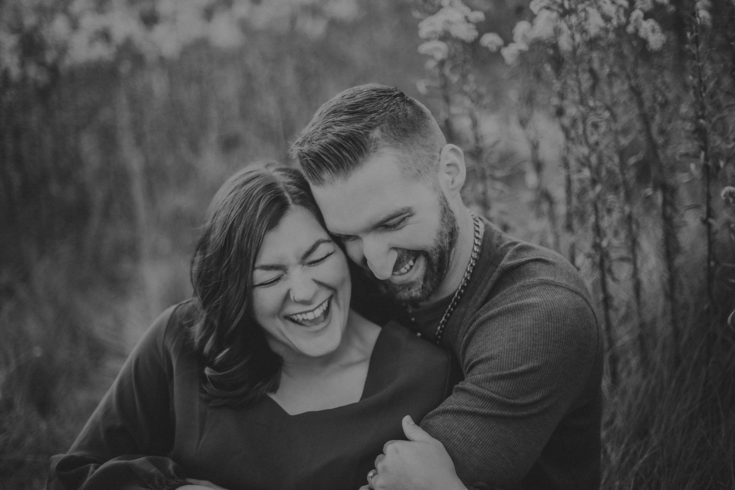 Black and white portrait of couple laughing together among wildflowers.