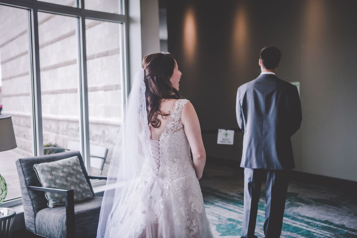 Bride and groom standing before large windows during their first look moment.