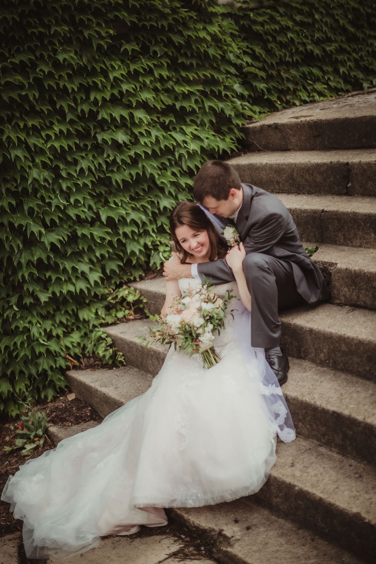 Candid wedding moment captured on ivy-covered stairs with bride holding romantic bouquet.