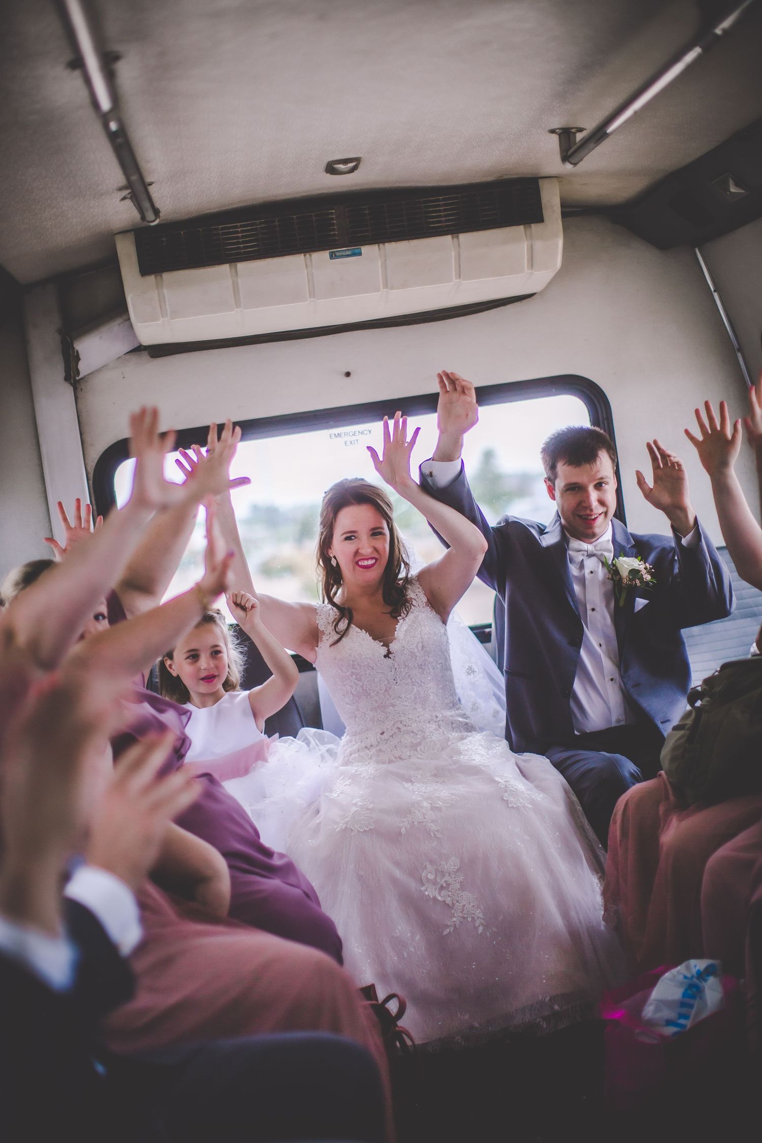 Wedding party celebrates with raised hands inside decorated party bus.