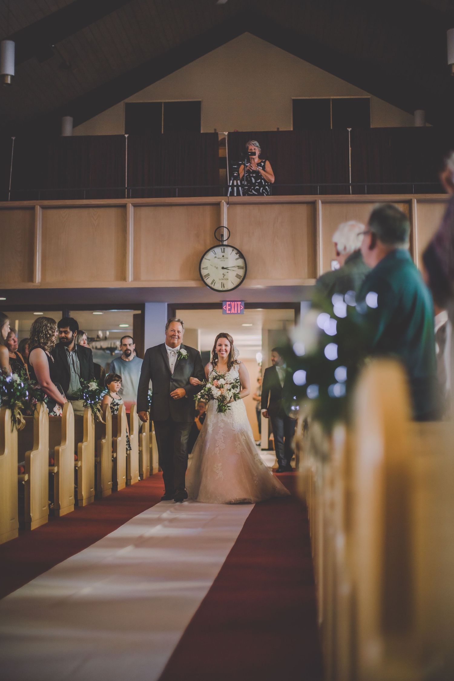 Church interior with wooden pews and red carpet aisle during wedding ceremony.