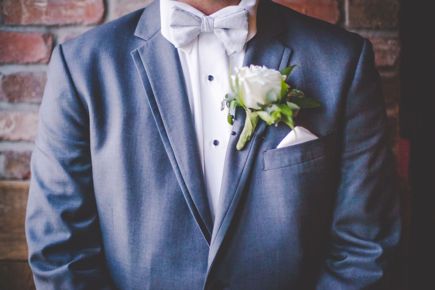 Close-up of a formal blue suit with white bow tie and rose boutonniere.