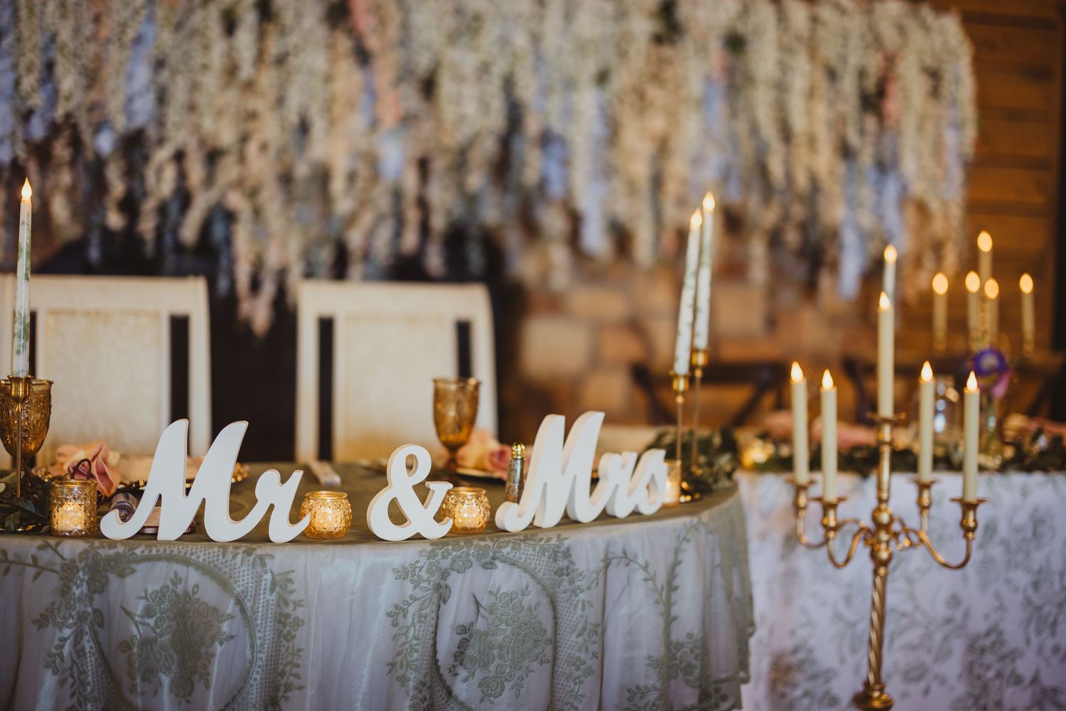 Elegant wedding sweetheart table with Mr & Mrs signs, gold candelabras, and floral ceiling decor.