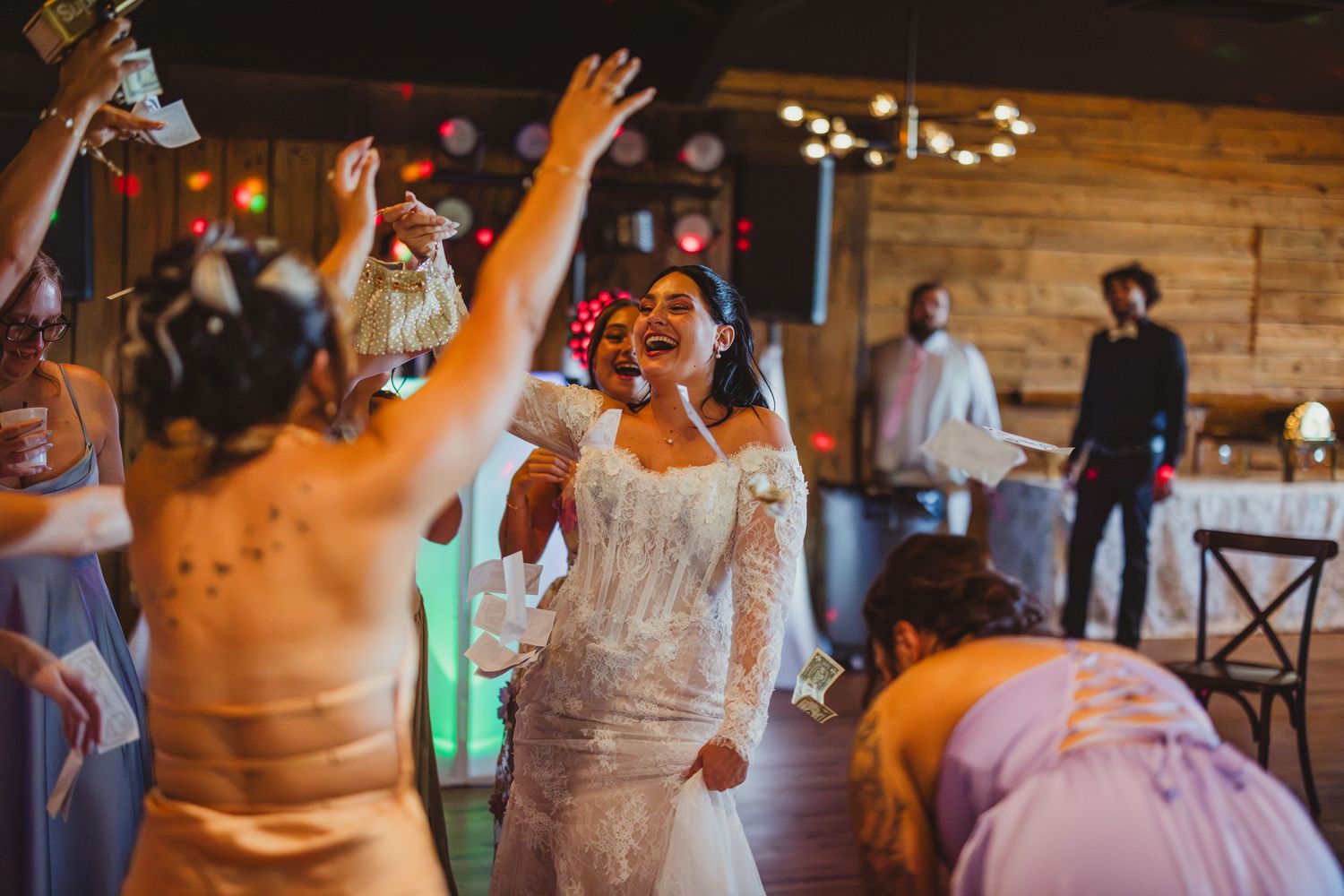Bride in white lace wedding gown laughing and dancing joyfully with guests at a vibrant wedding reception.