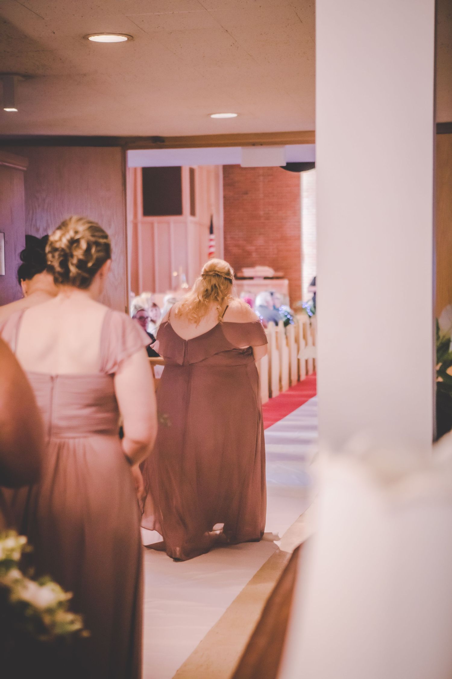 Bridesmaids in matching brown dresses line up in a church corridor.
