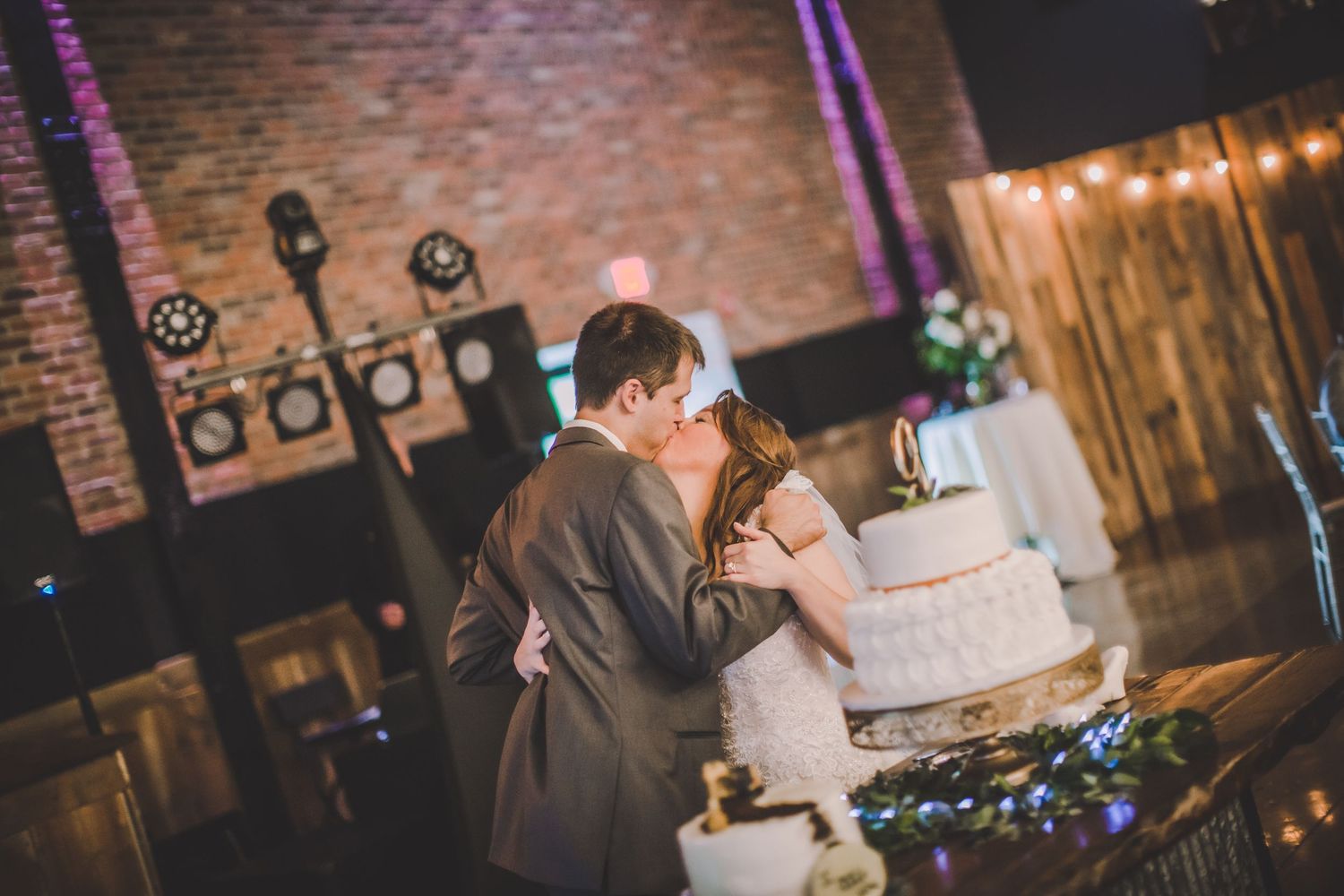 A couple embraces while cutting their three-tiered white wedding cake at their reception.