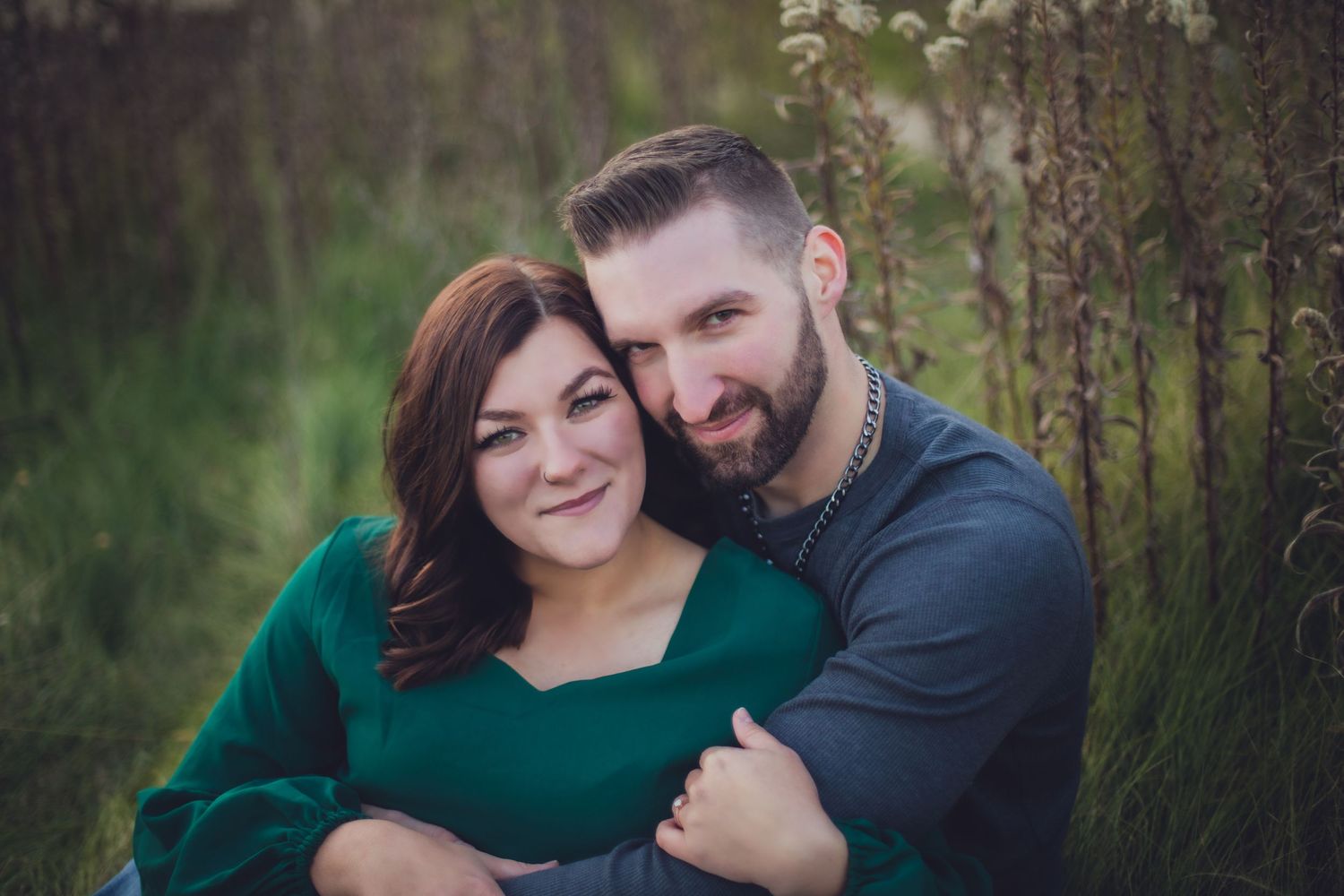 Intimate portrait of couple in green sweater and blue shirt among tall grass.