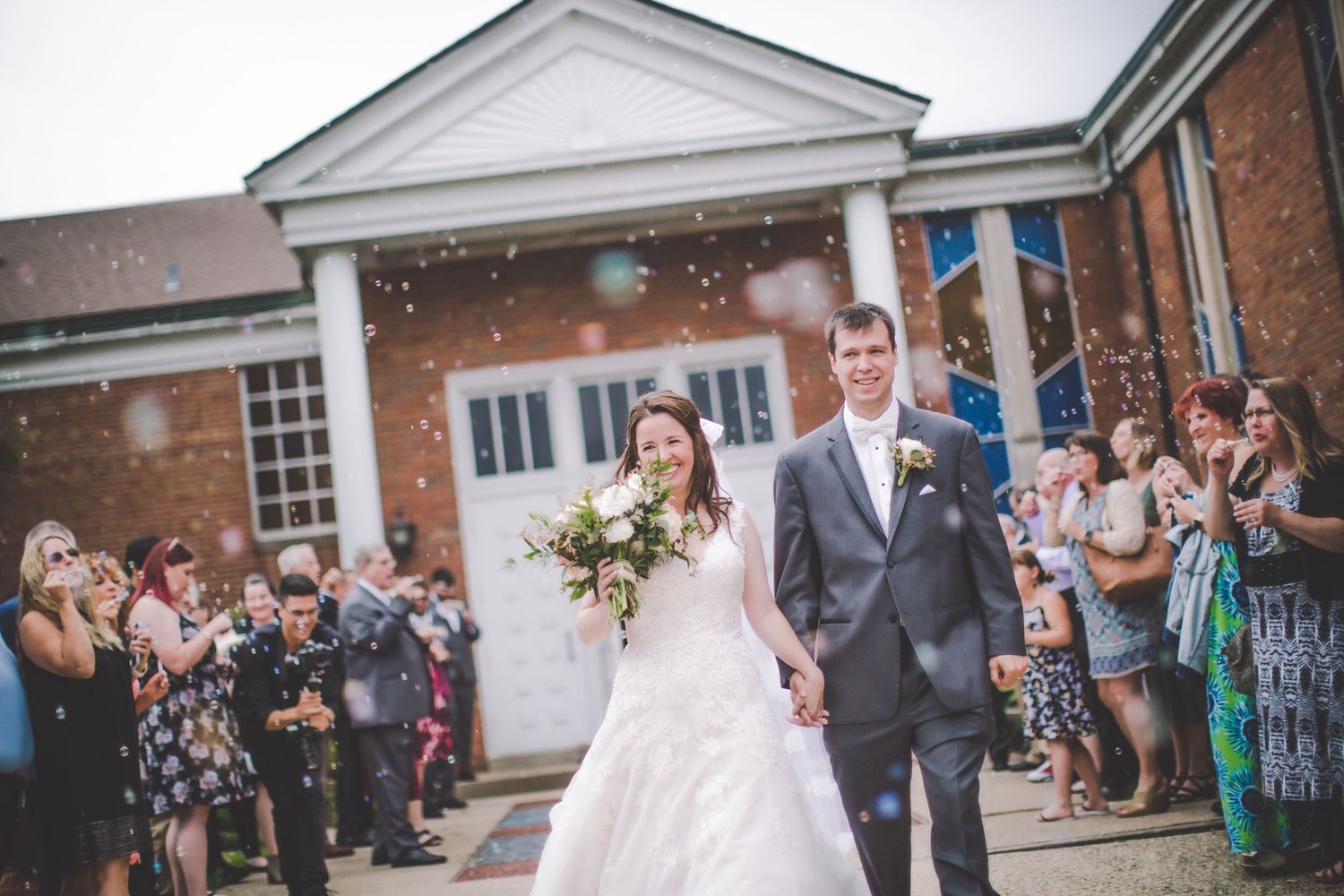 Wedding celebration with confetti toss outside historic brick building entrance.