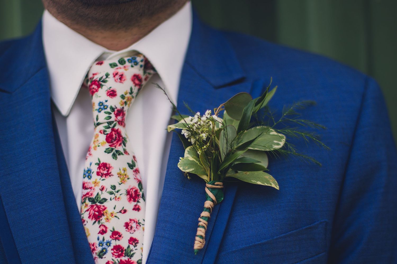 Detail shot of bright blue suit jackets with pink floral ties and greenery boutonnieres.