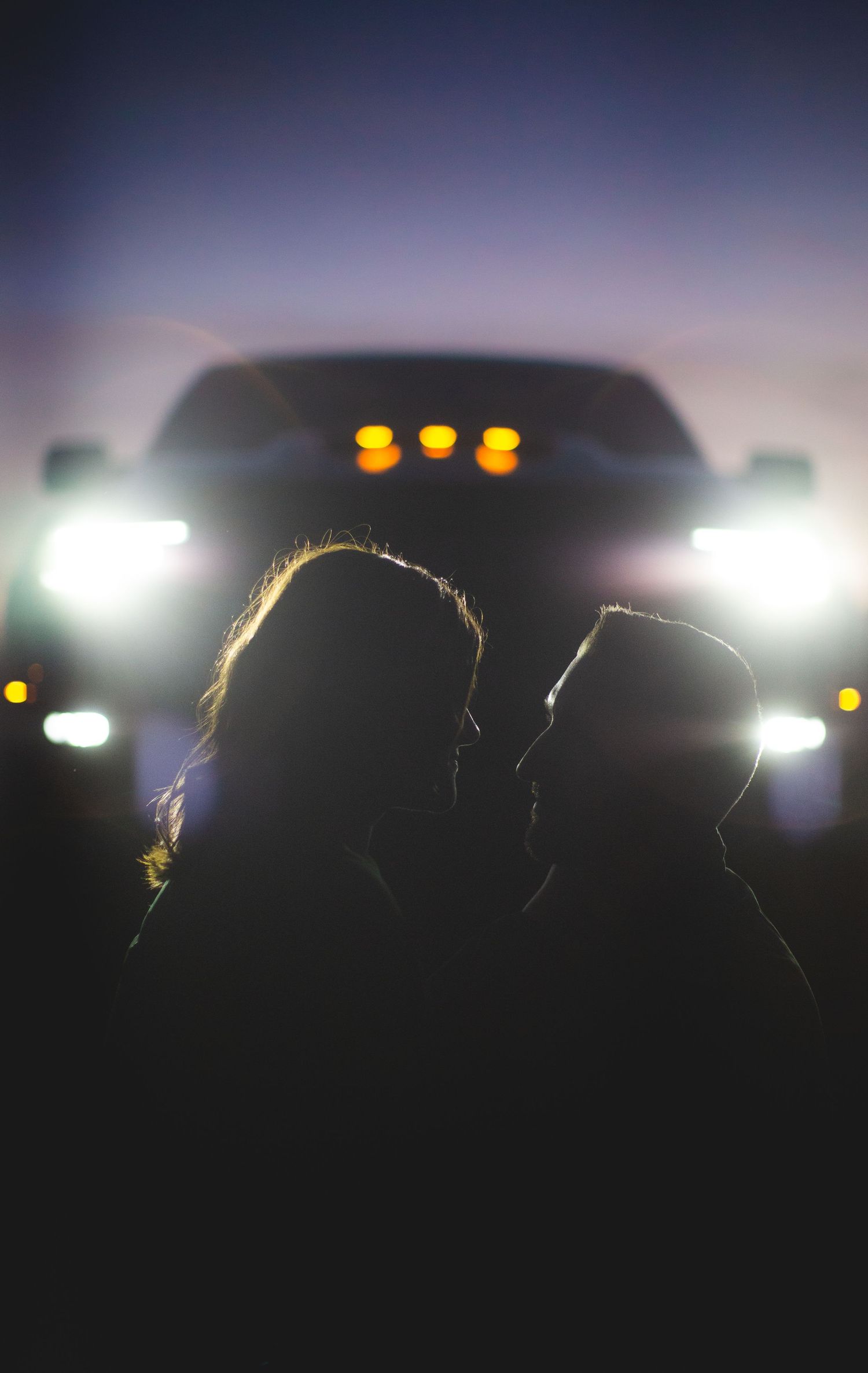 Backlit couple's silhouette with car headlights creating dramatic evening atmosphere.