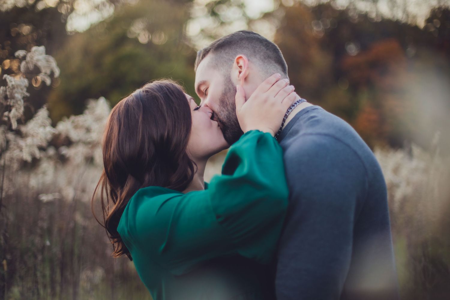Couple sharing passionate kiss in field of dried flowers at golden hour.