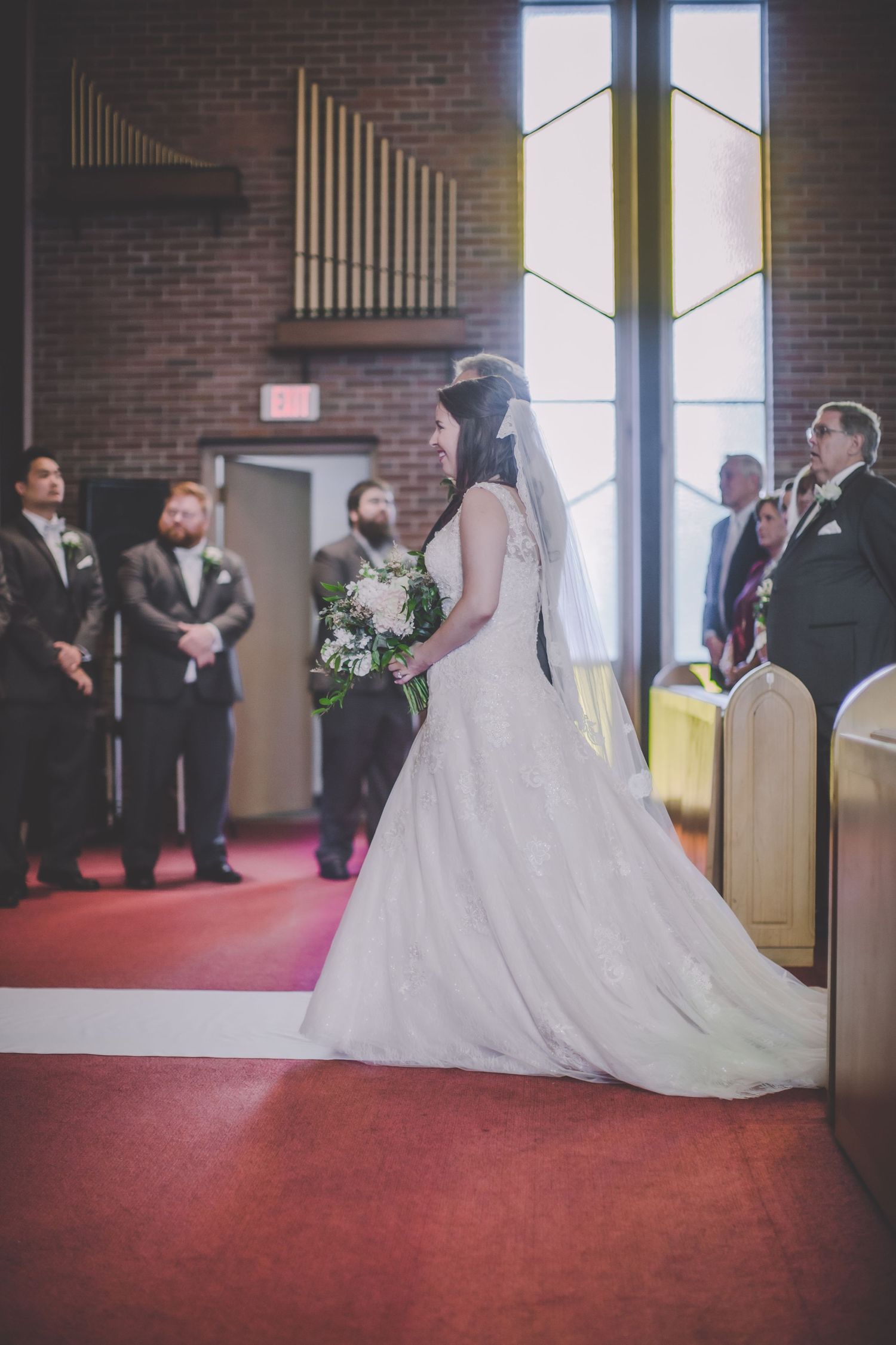 Wedding ceremony taking place in traditional church setting with red carpet and brick walls.