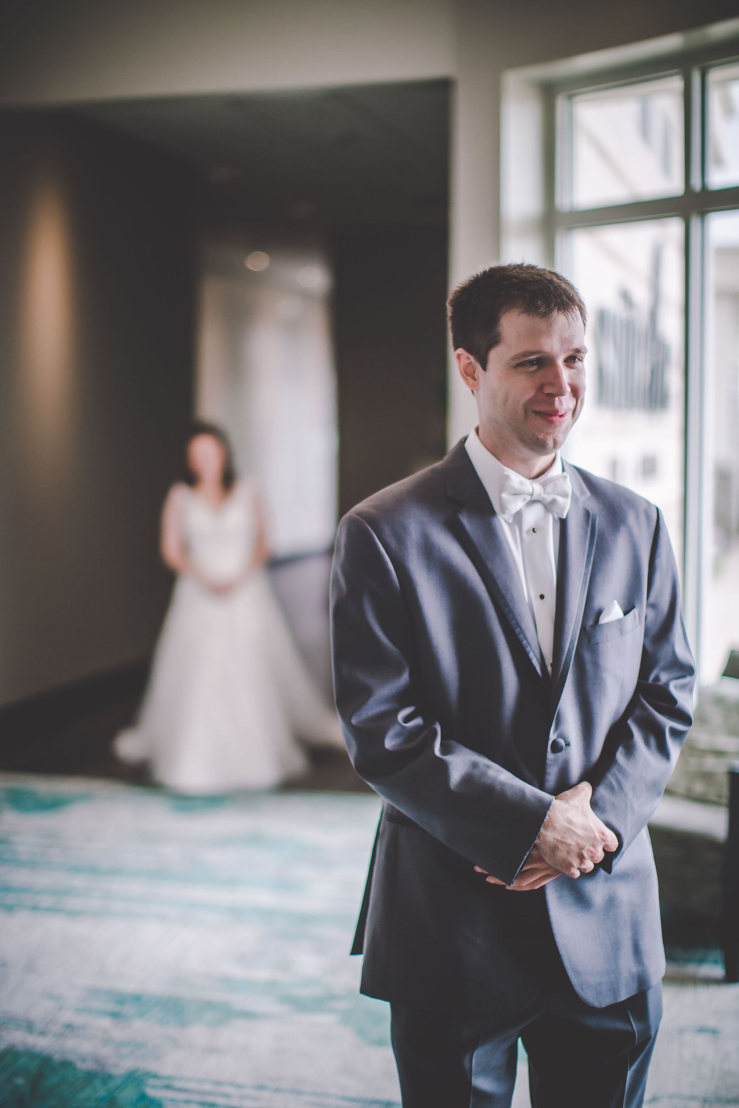Wedding portrait showing formal attire with figure in white dress in background.