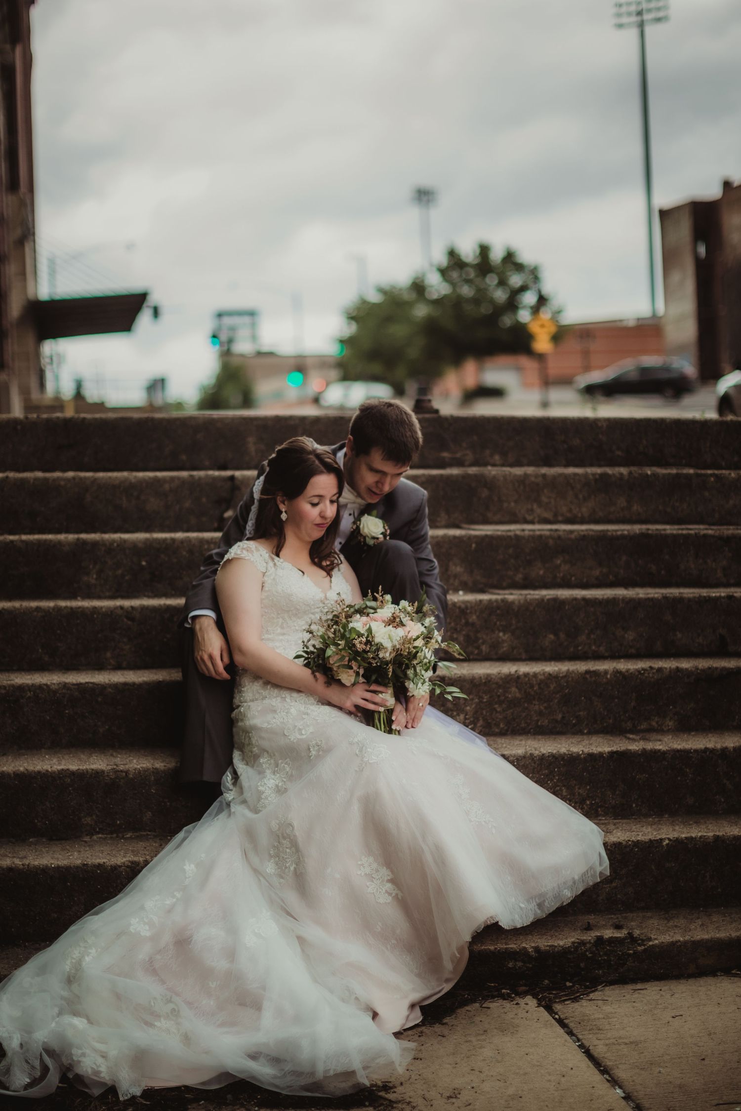 Wedding couple embraces on concrete steps against an industrial urban background.