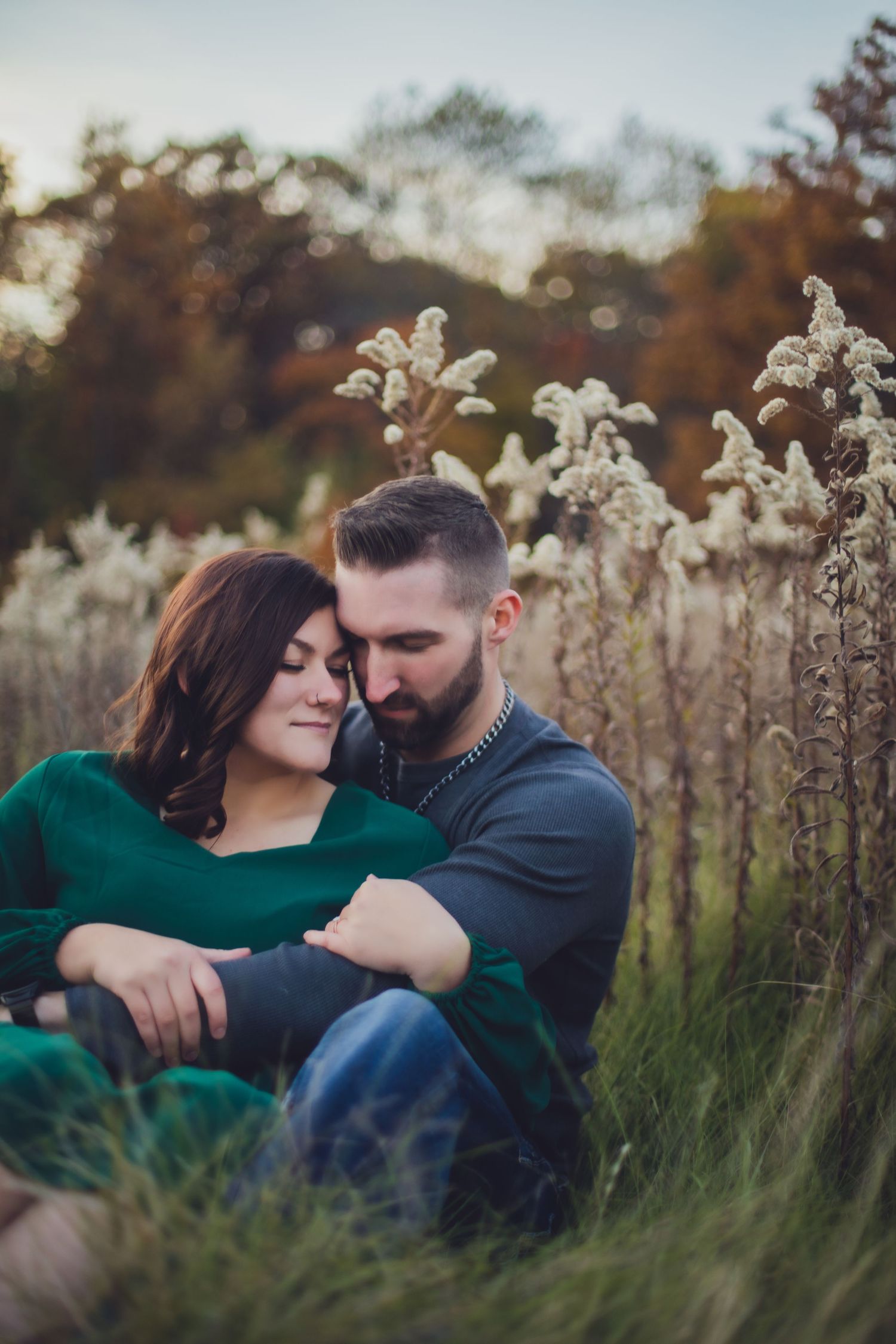 Romantic couple embraces in a field of tall grass and wildflowers during golden hour.