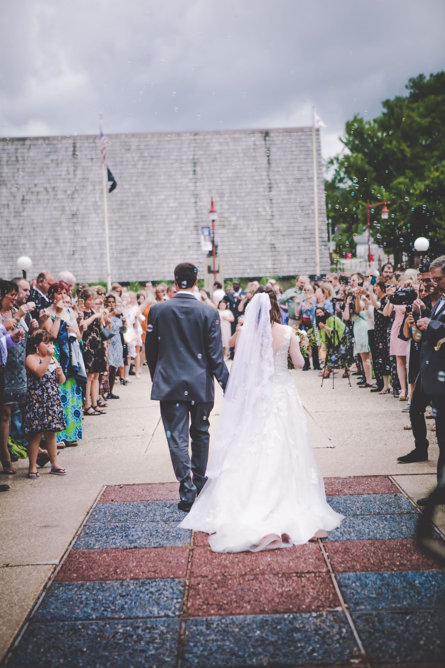 Wedding celebration in front of a white stone wall with guests lined up on both sides of a red and blue carpet.