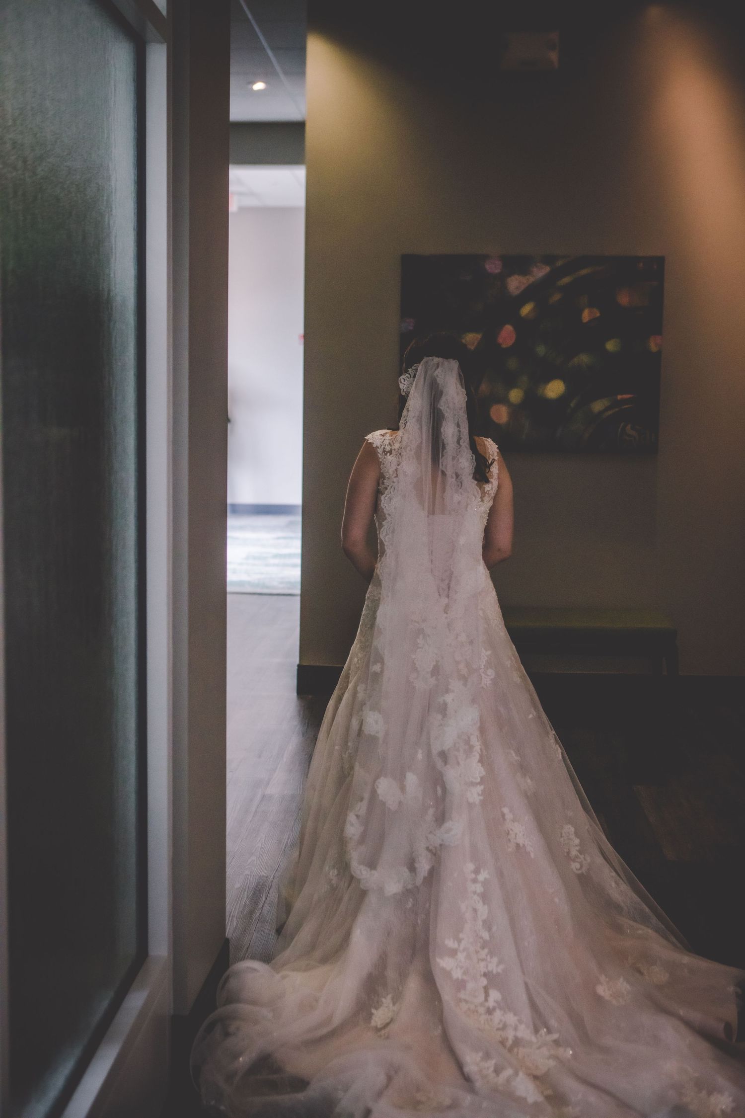 Back view of a lace wedding dress with cathedral train in a modern hallway.
