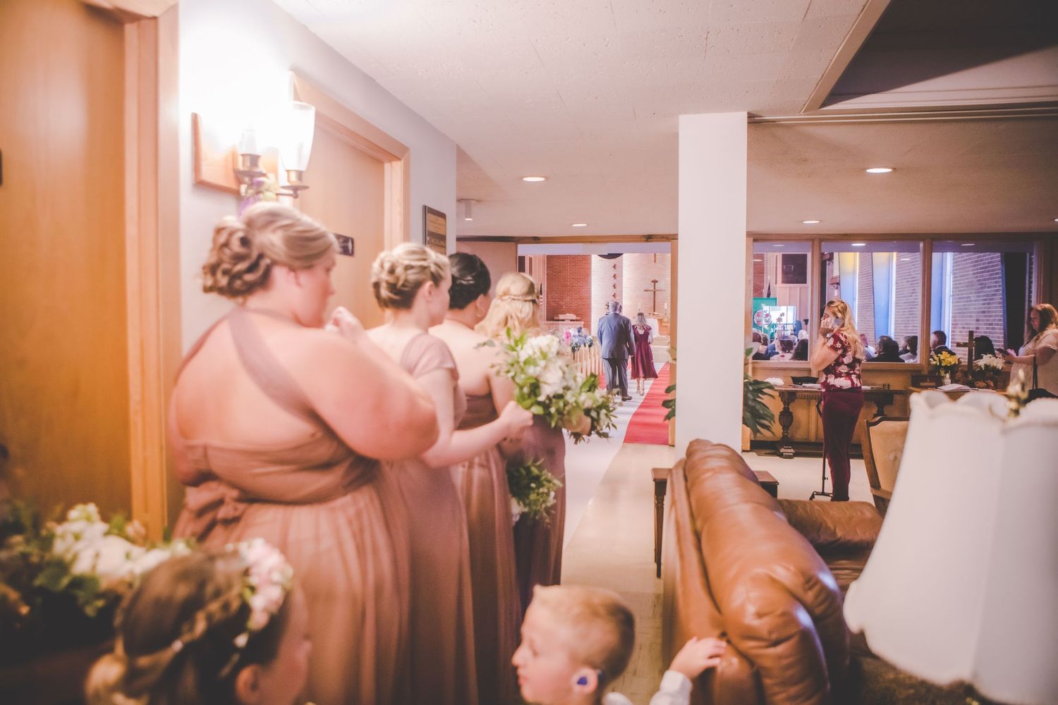 Wedding party members in pink dresses gather in hallway before ceremony.