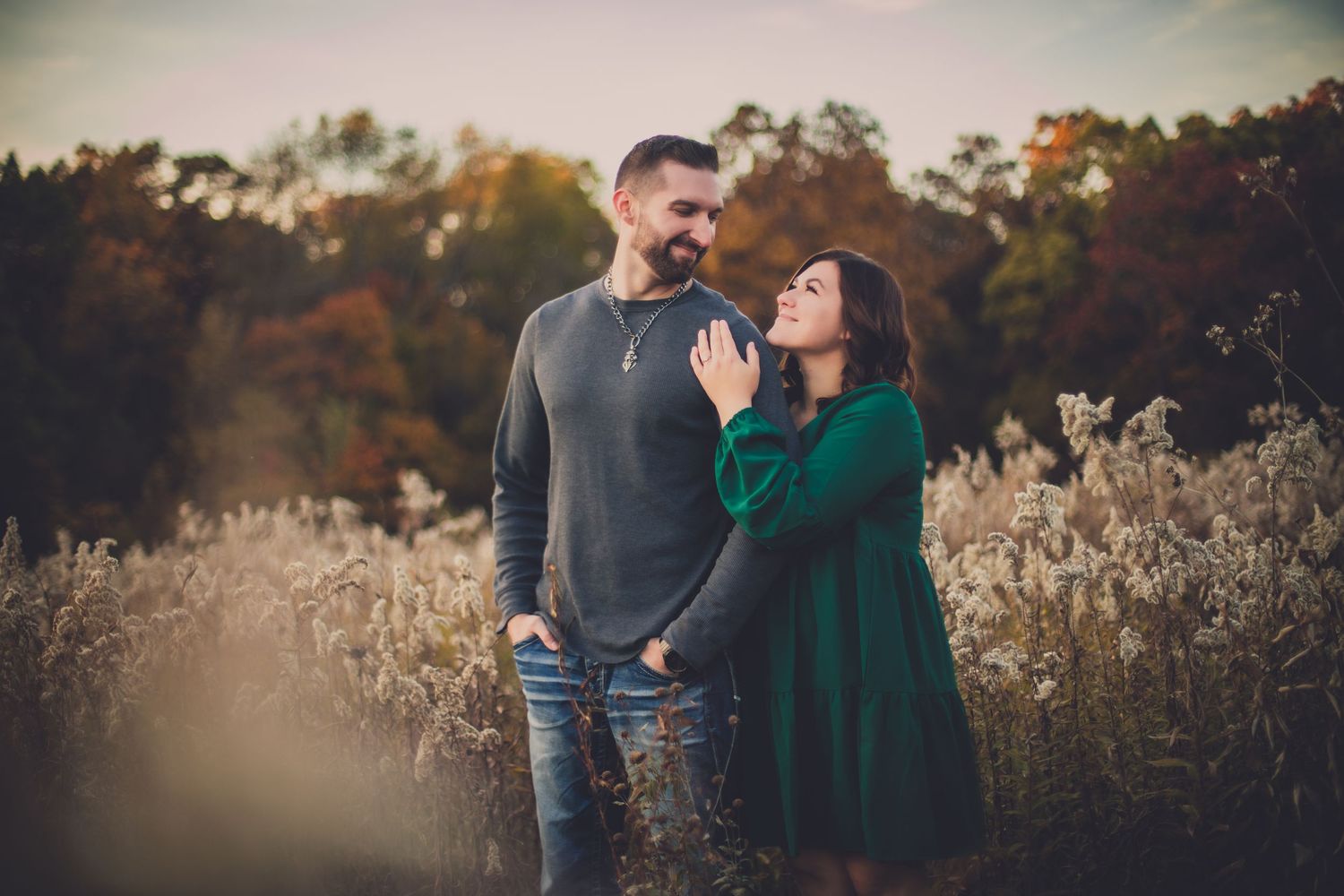 Tender moment between couple wearing grey and green in autumn field setting.