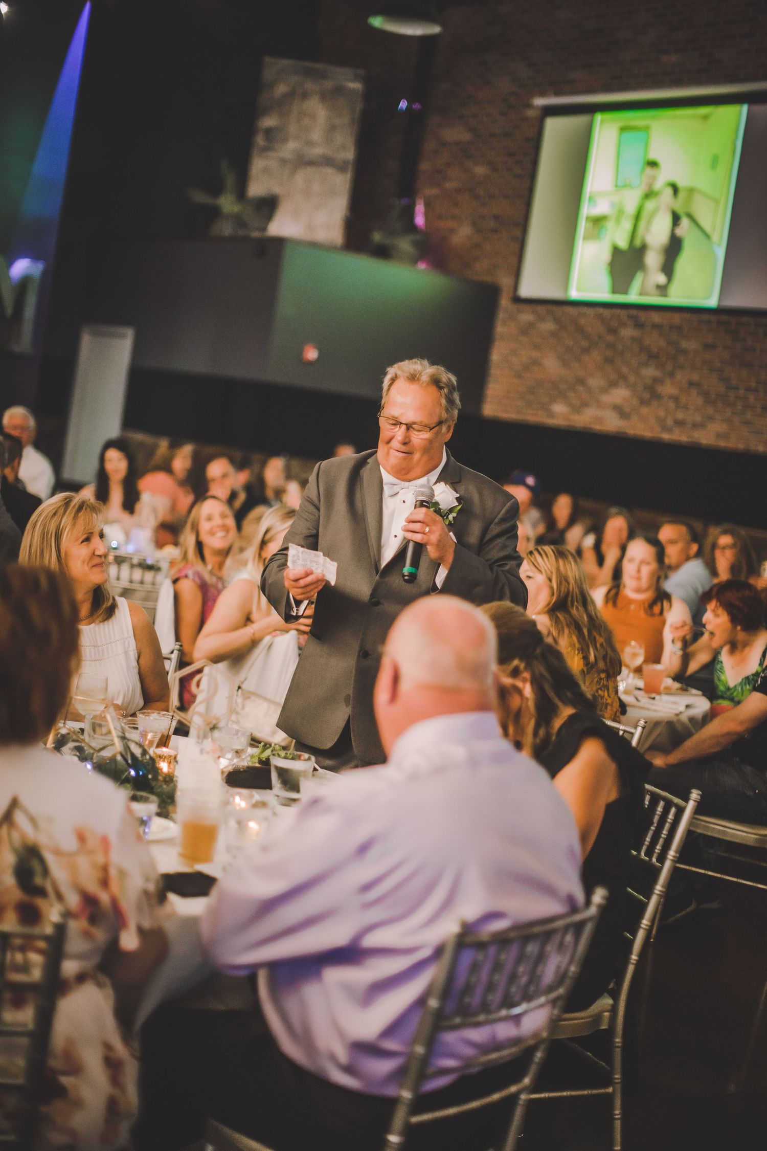 A person gives an emotional speech at a wedding reception while guests watch from decorated dining tables.