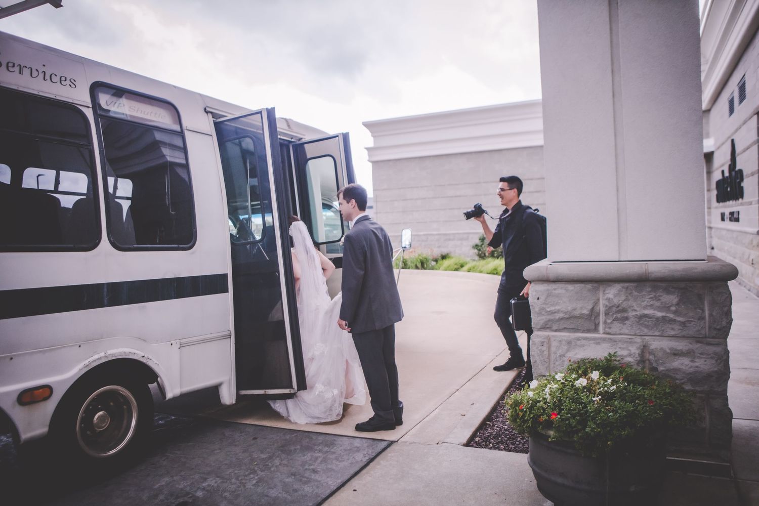 Wedding party members boarding a white shuttle bus or party vehicle.