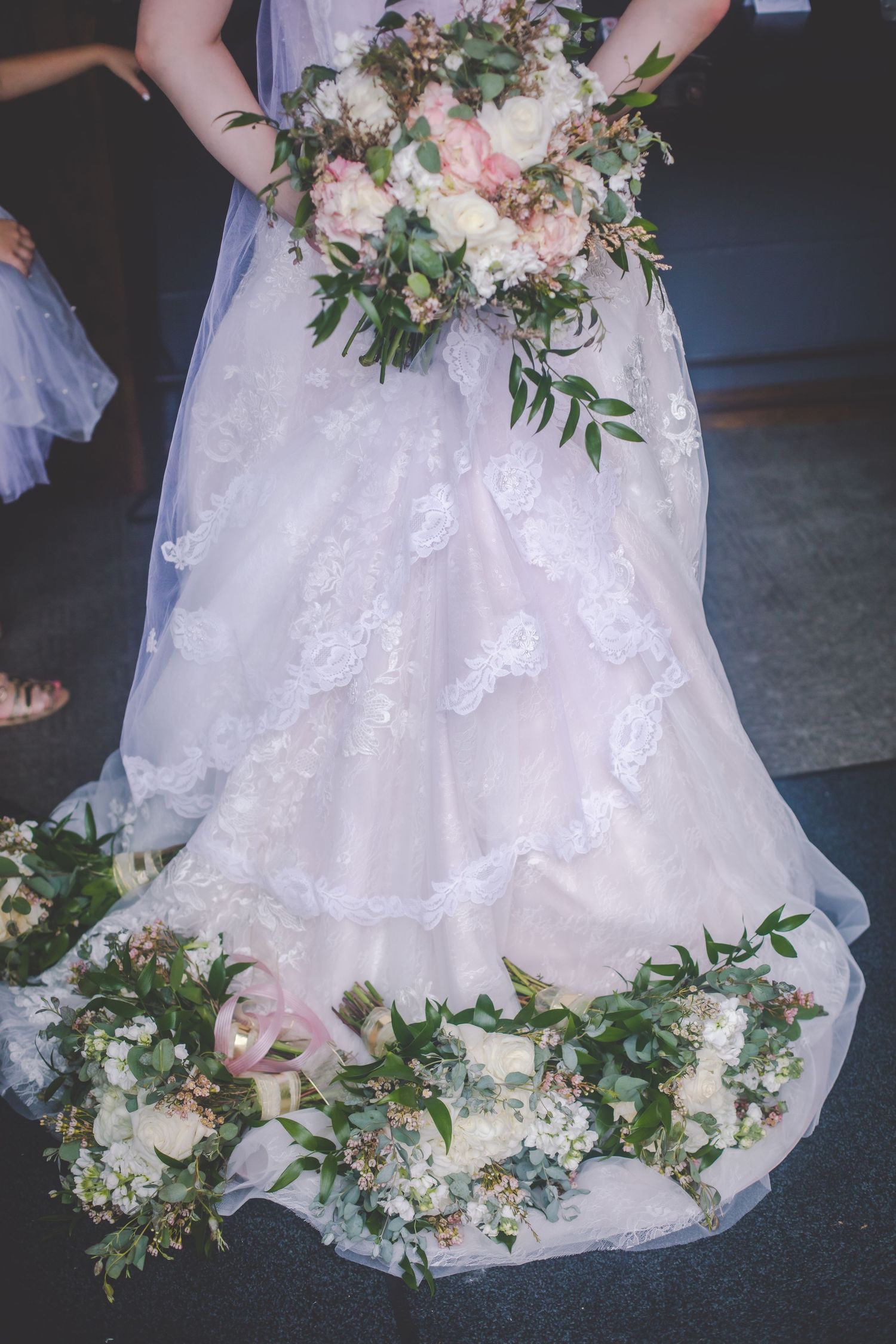 Detailed view of a white lace wedding dress adorned with floral arrangements at the hem.