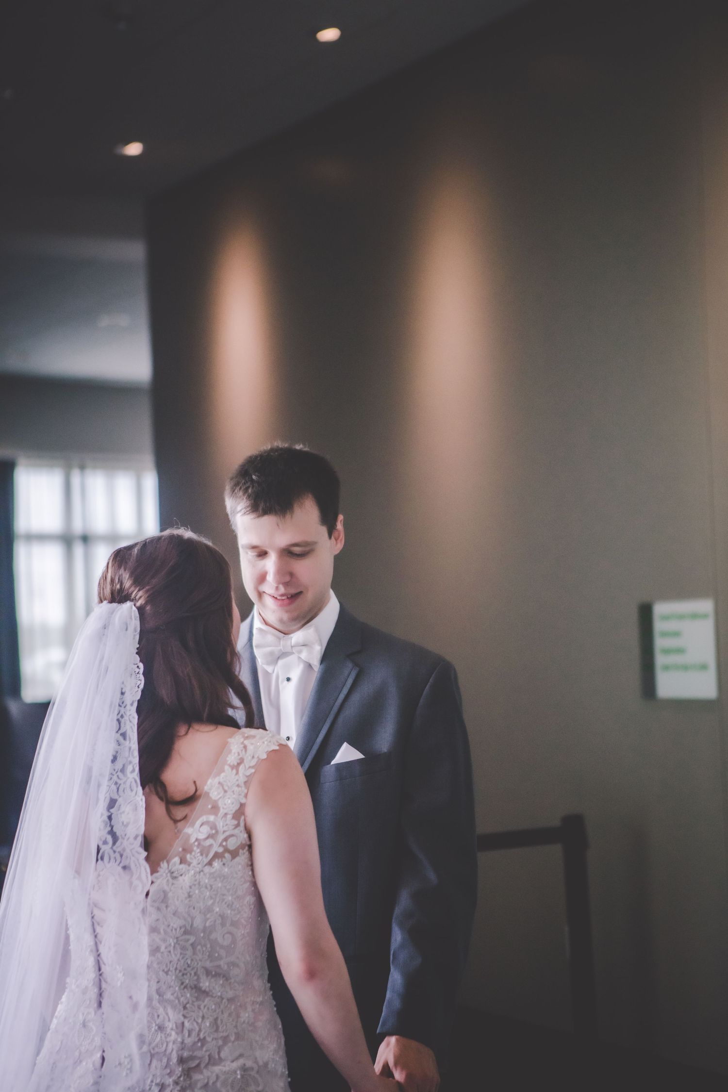 A tender first look moment between newlyweds in a dimly lit hallway.