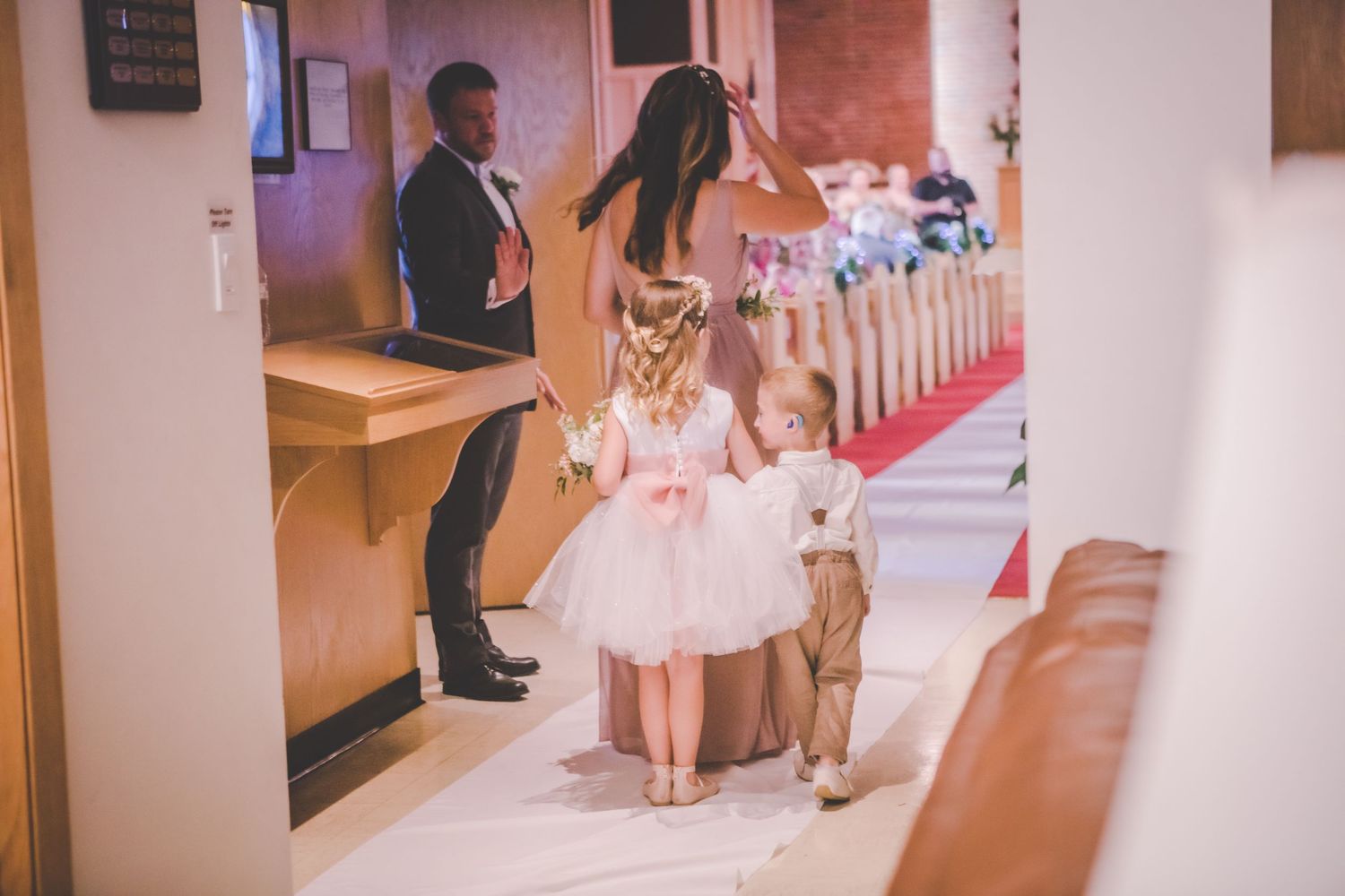 Wedding party members walk through a church hallway with red carpet.