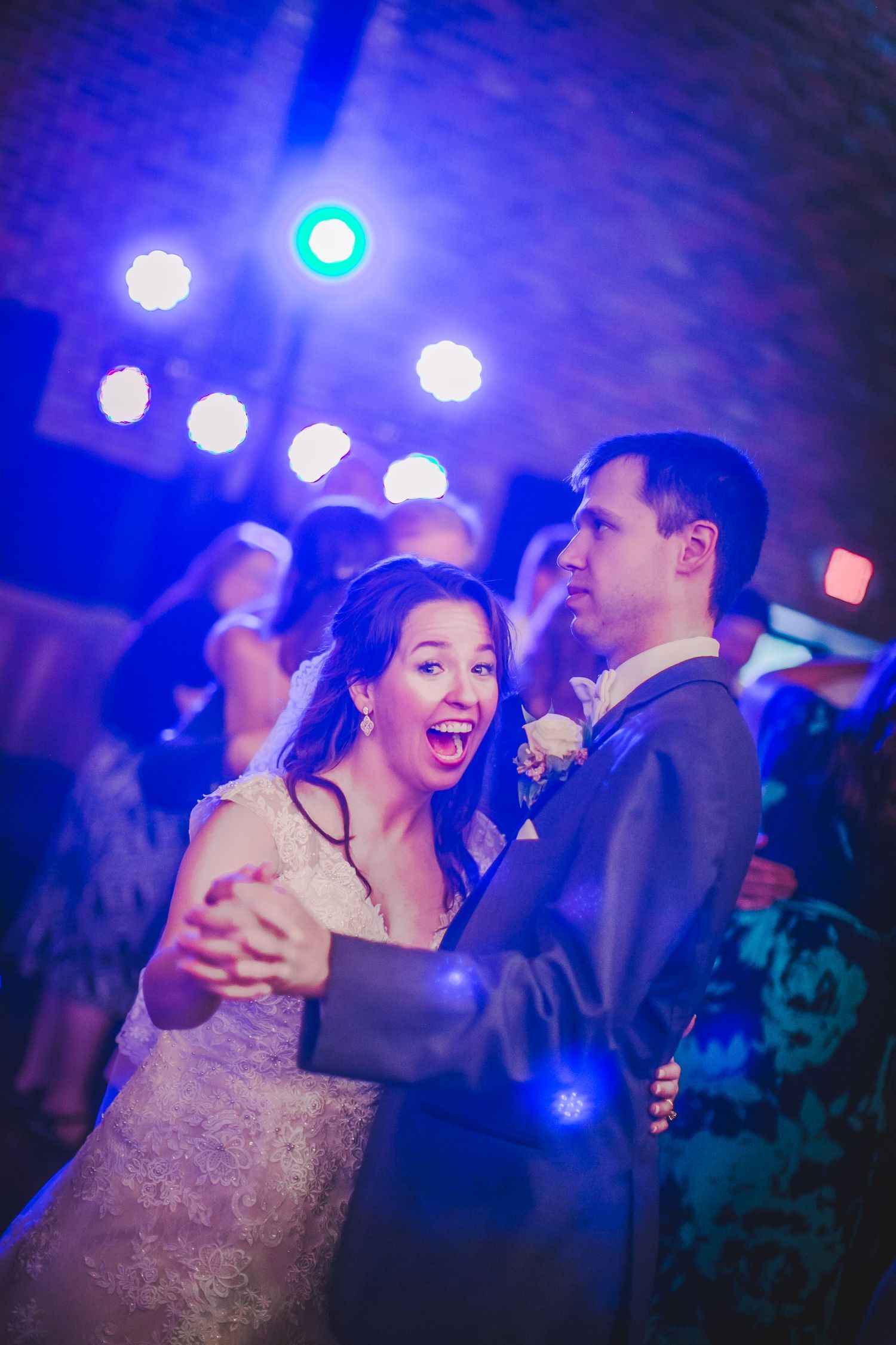 Dancing couple captured in a candid moment under blue lighting at their wedding celebration.