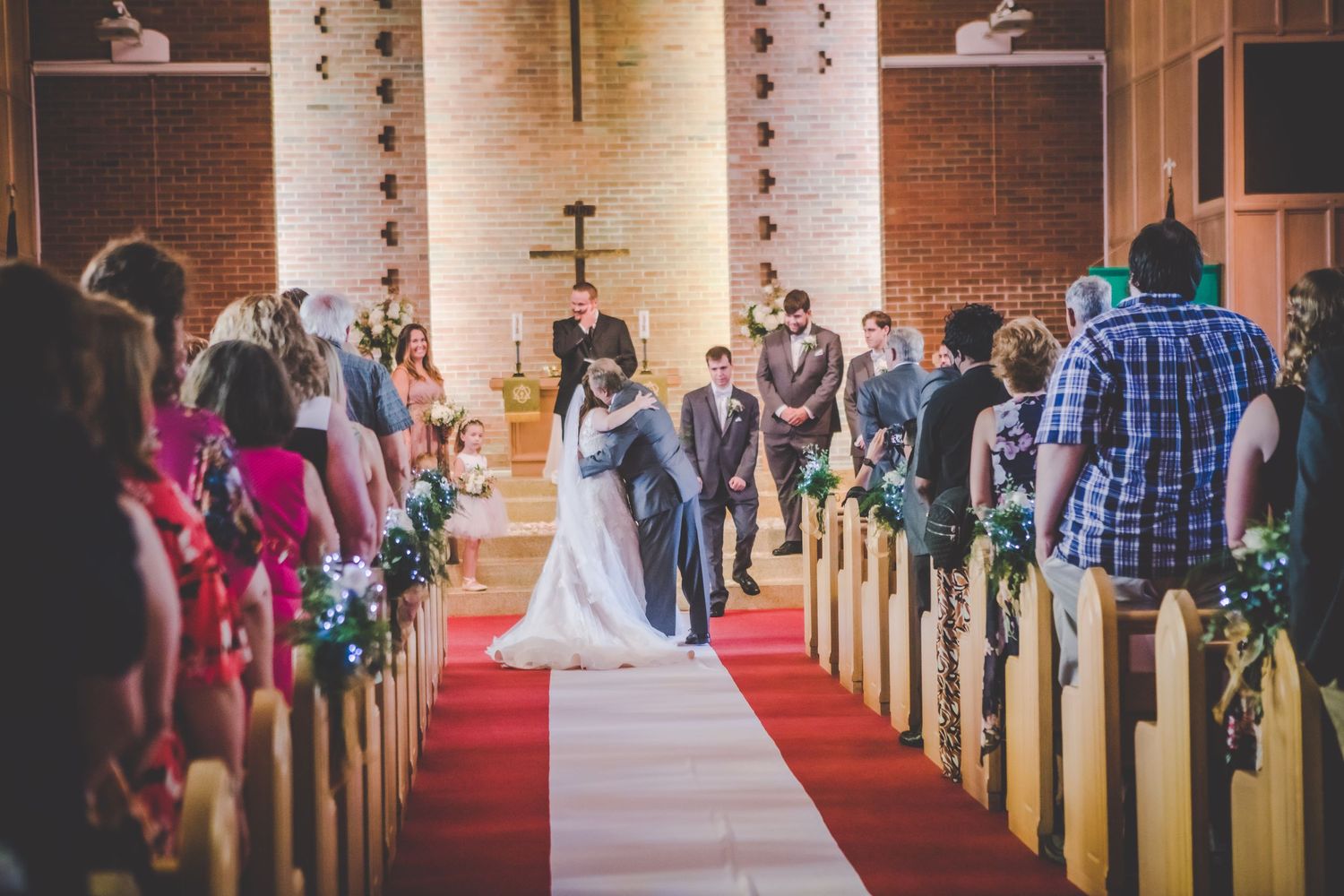 Wedding ceremony underway in traditional church sanctuary with brick walls and wooden pews.