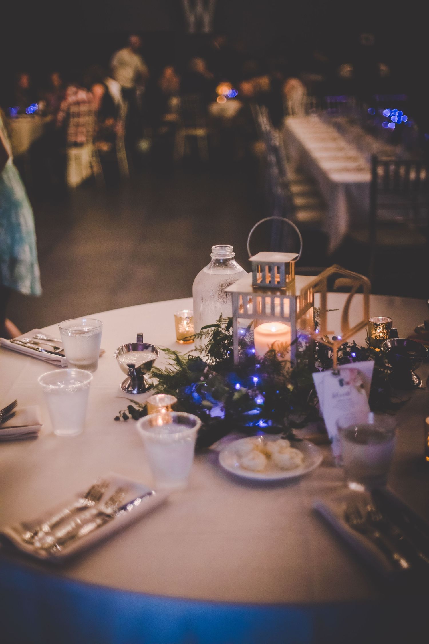 An elegantly decorated reception table with lantern centerpiece and blue ambient lighting.