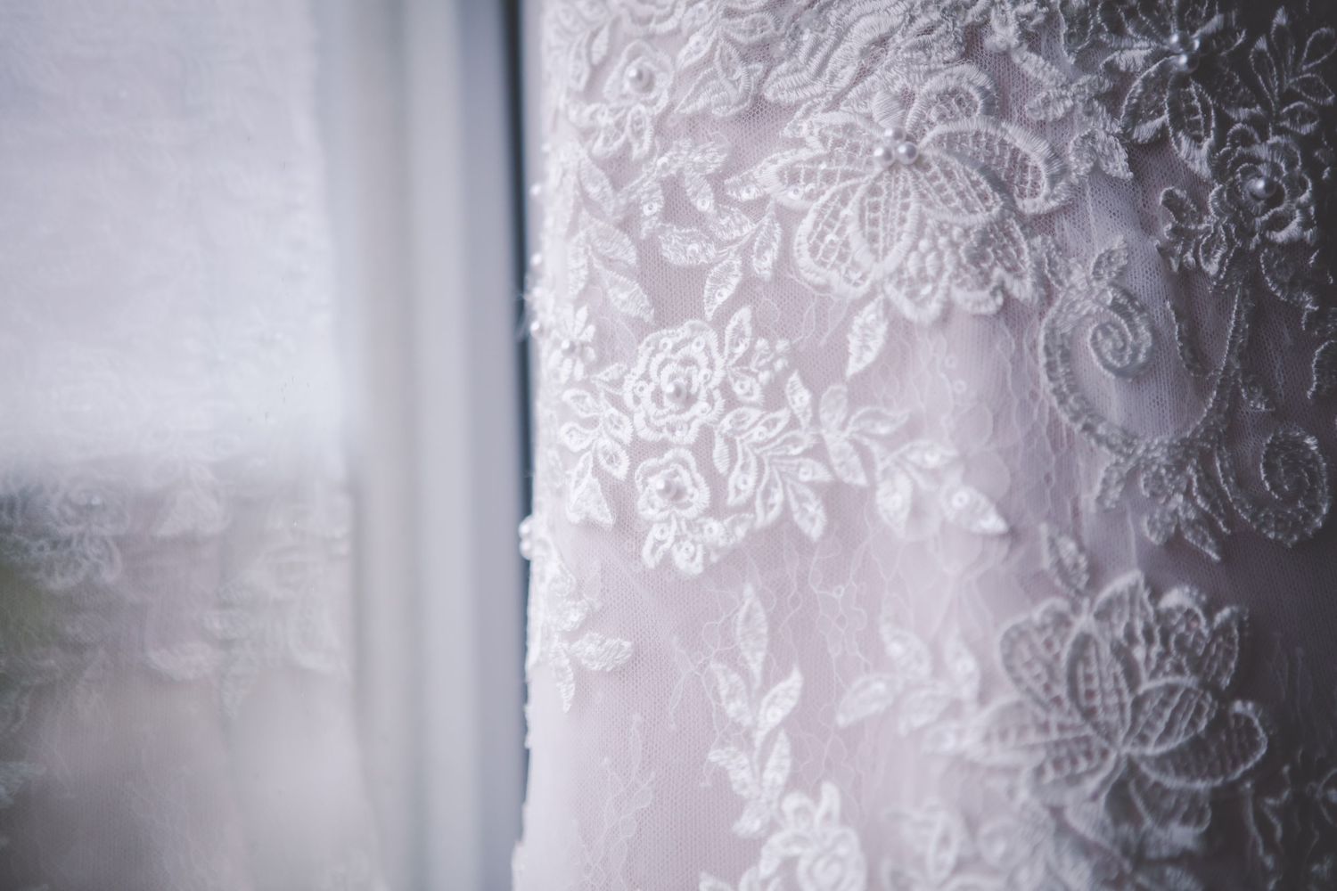 Close-up detail of white lace and beadwork pattern on a wedding gown.