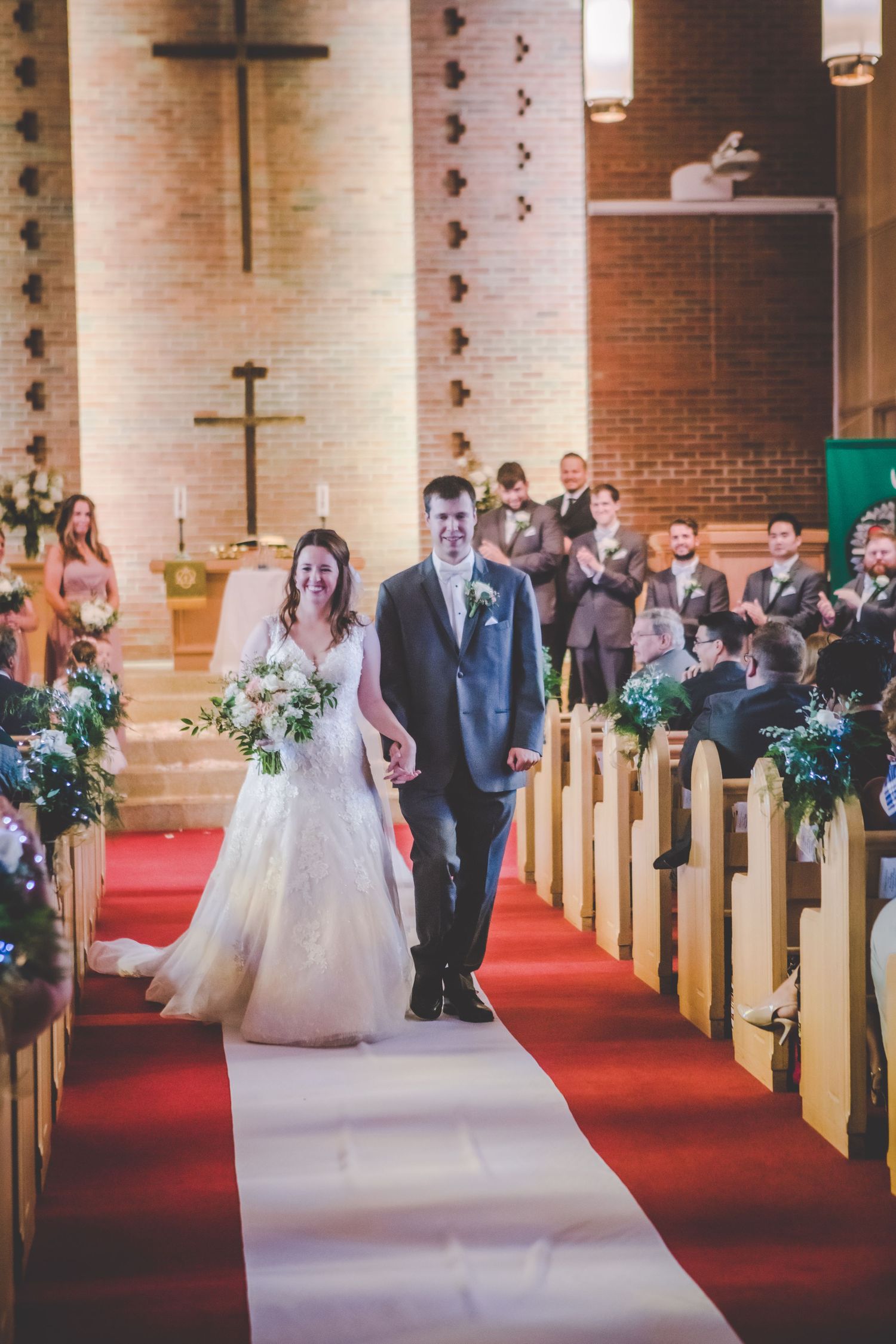 Wedding ceremony procession in a brick church with floral decorations on pews.