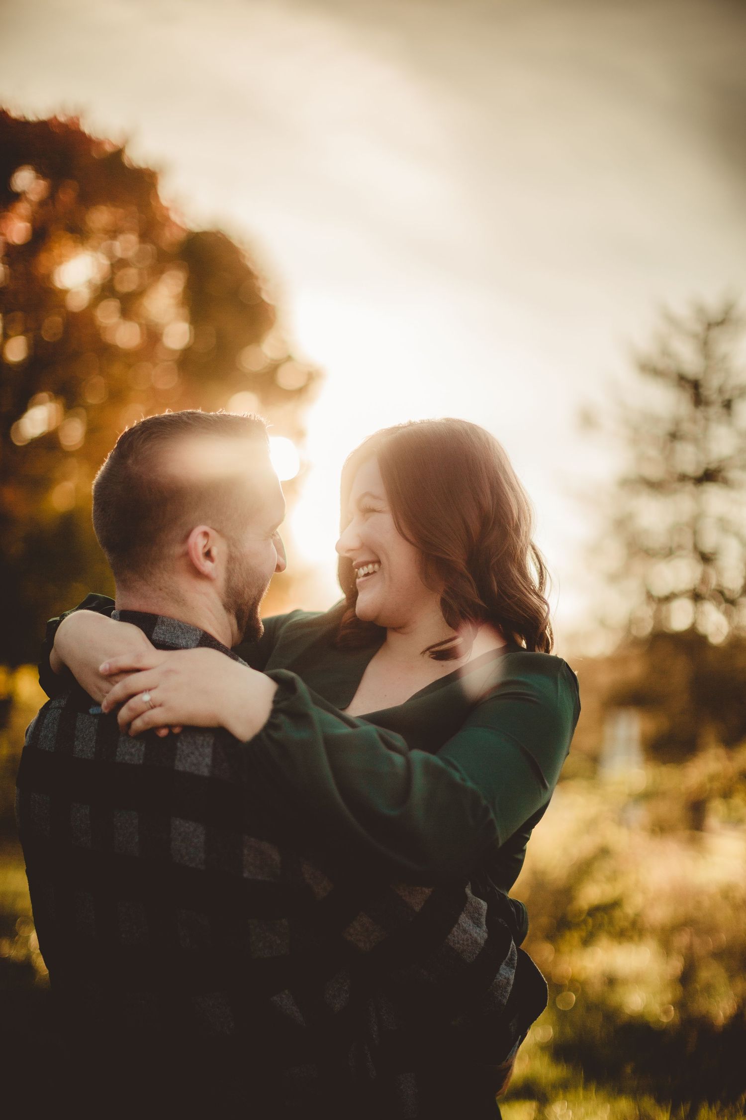 Sunlit autumn engagement photo with warm golden tones and natural backlighting.