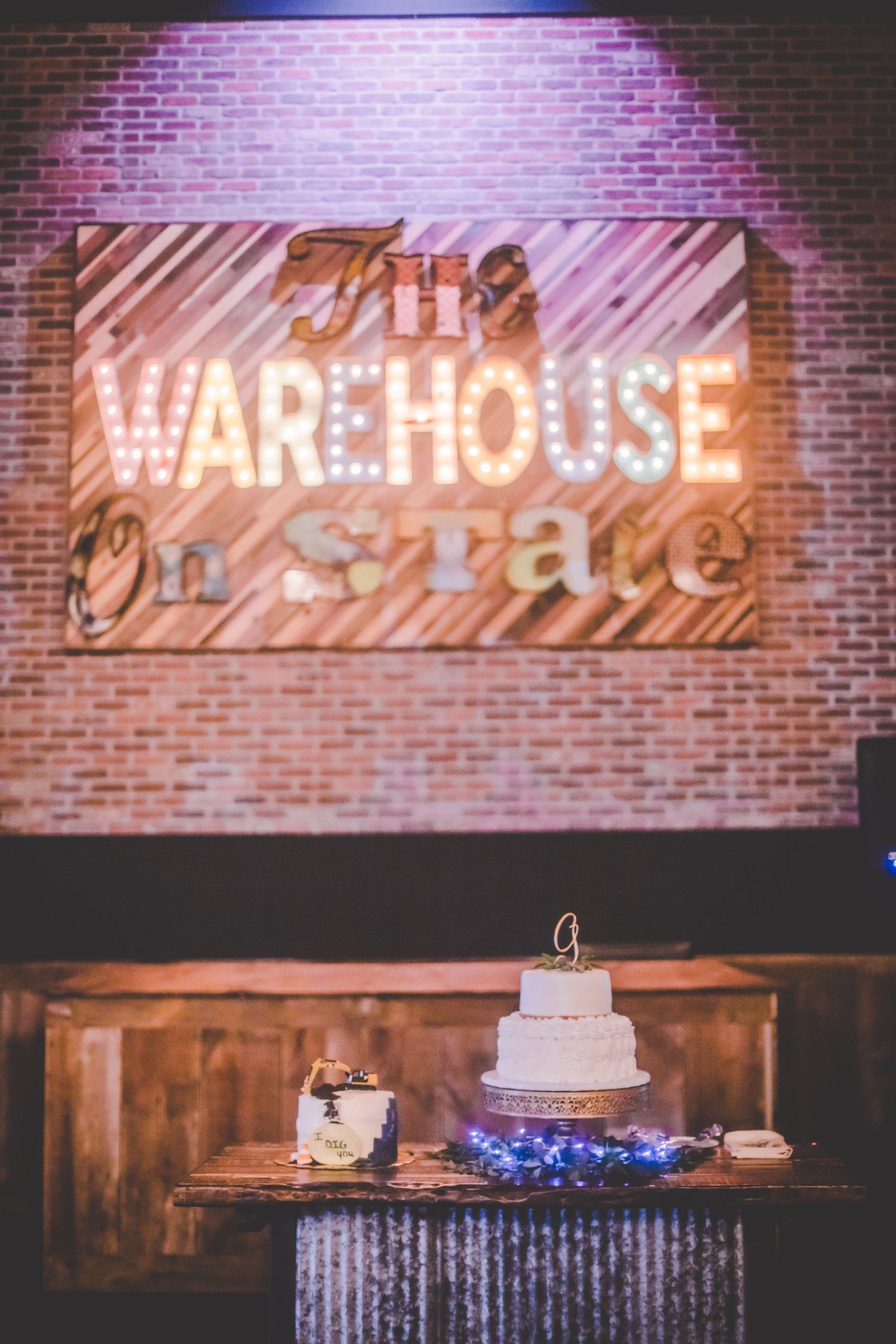 Vintage-style wedding venue with illuminated Warehouse signage and wedding cake display beneath.