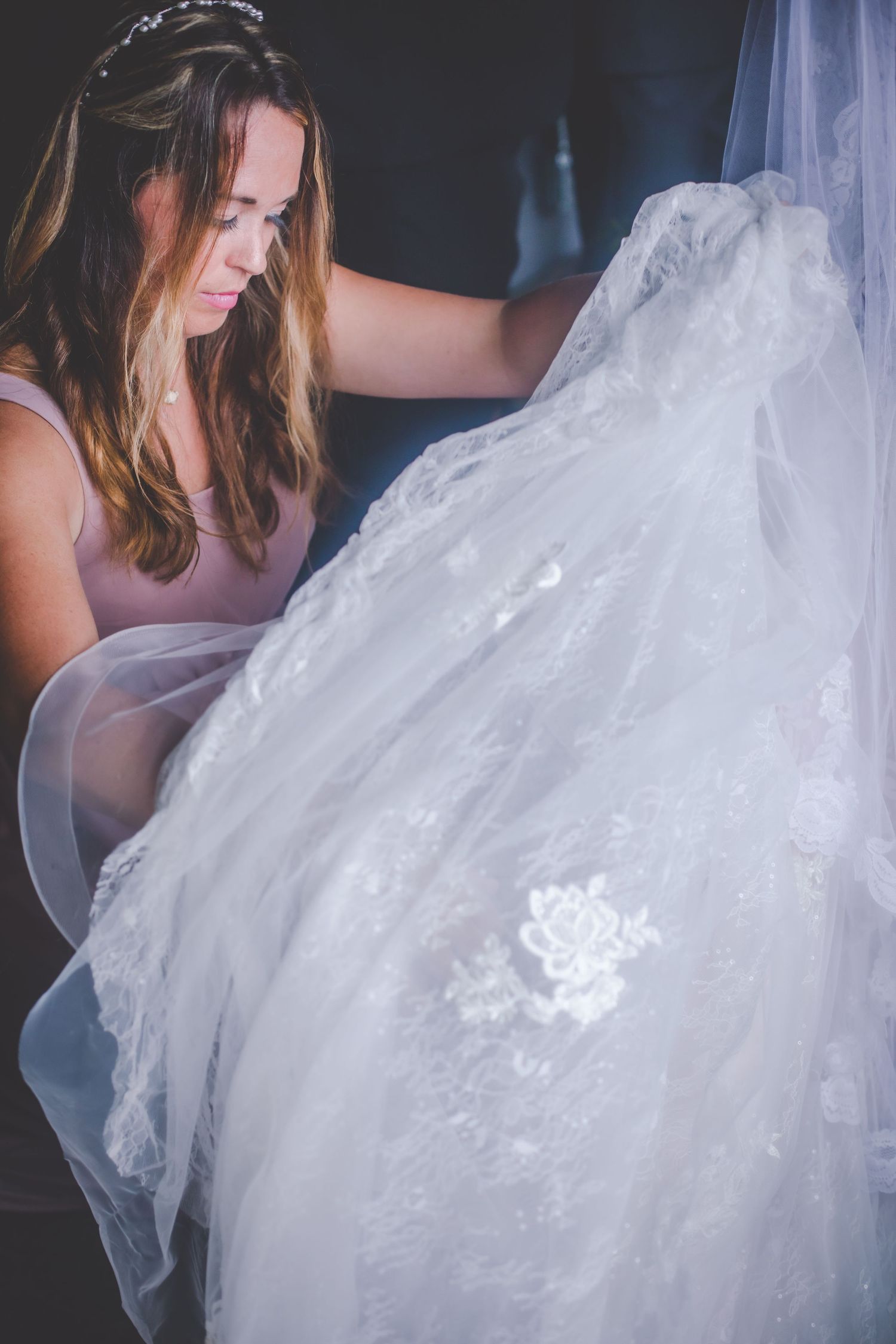 A delicate white lace wedding dress being adjusted with careful attention.